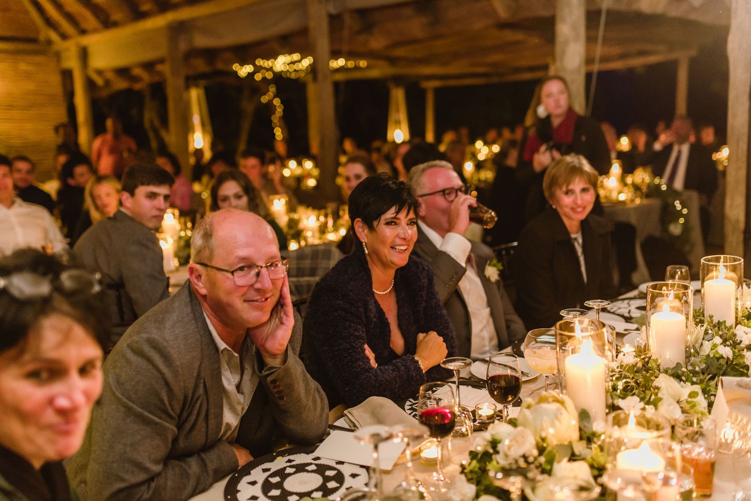 Wedding guests enjoying dinner at a candlelit reception with rustic barn-style decor.