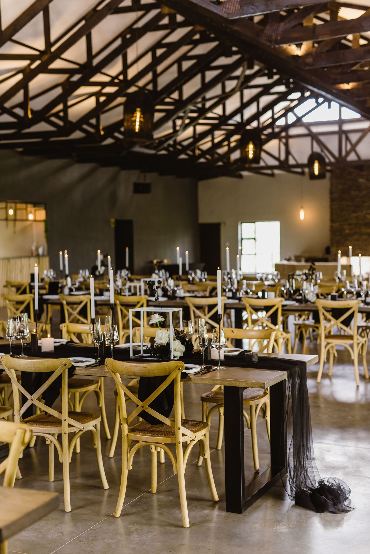Spacious wedding venue with rustic wooden crossback chairs and exposed beam ceiling.