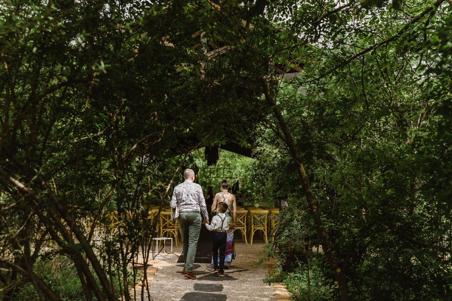 Wedding party members walking through lush garden pathway.