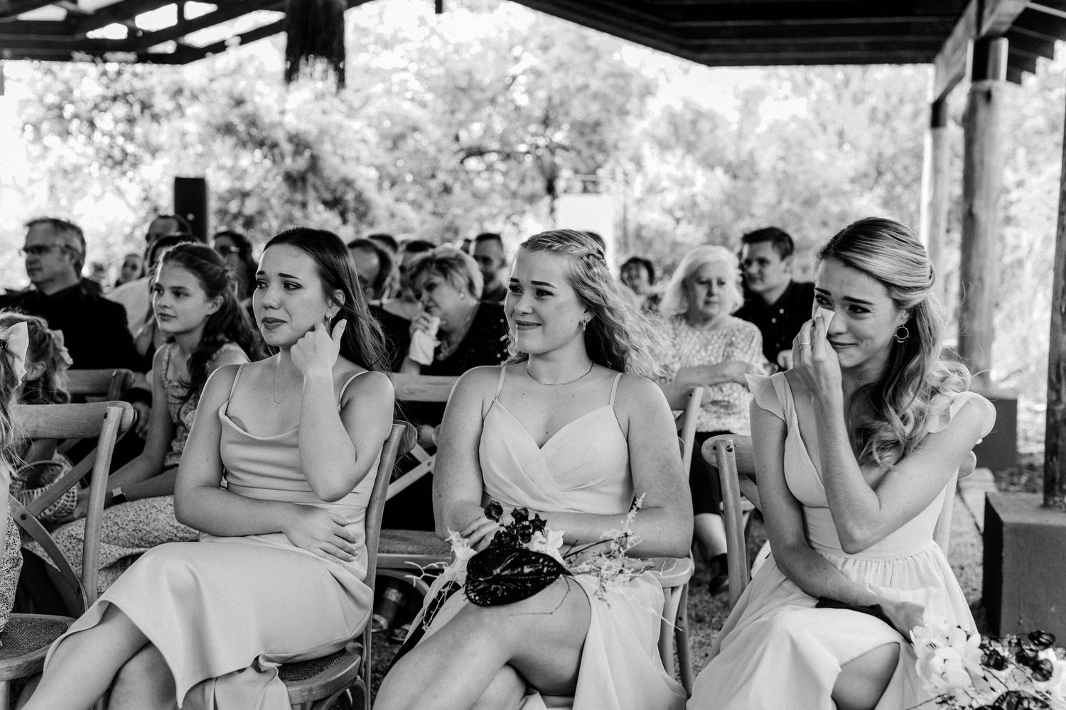 Guests seated at an outdoor wedding venue under a rustic covered pavilion.