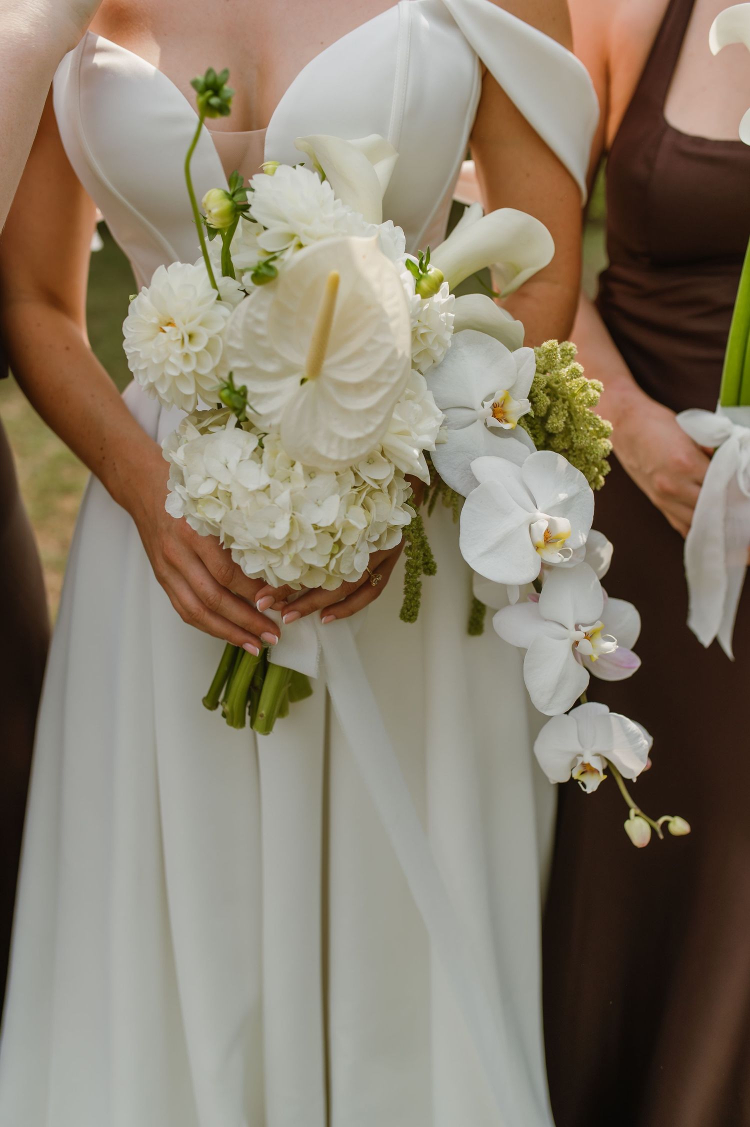 Row of elegant white and brown bridesmaid bouquets featuring orchids and hydrangeas held at waist level.