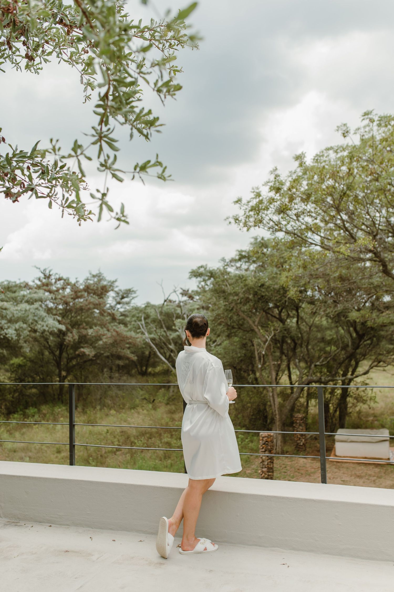 A person in white walks on an outdoor terrace overlooking a scenic landscape with trees.