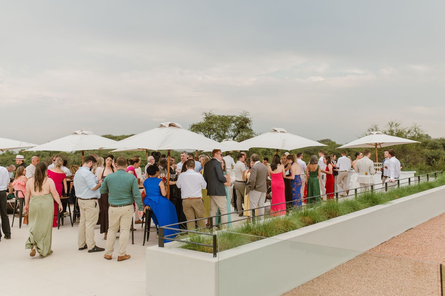 Panoramic view of an outdoor wedding reception with white umbrellas and guests mingling on a grassy lawn.
