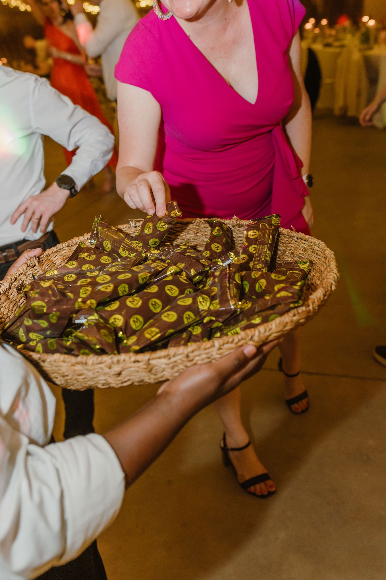 Server carrying a large woven basket of appetizers at an evening wedding reception.