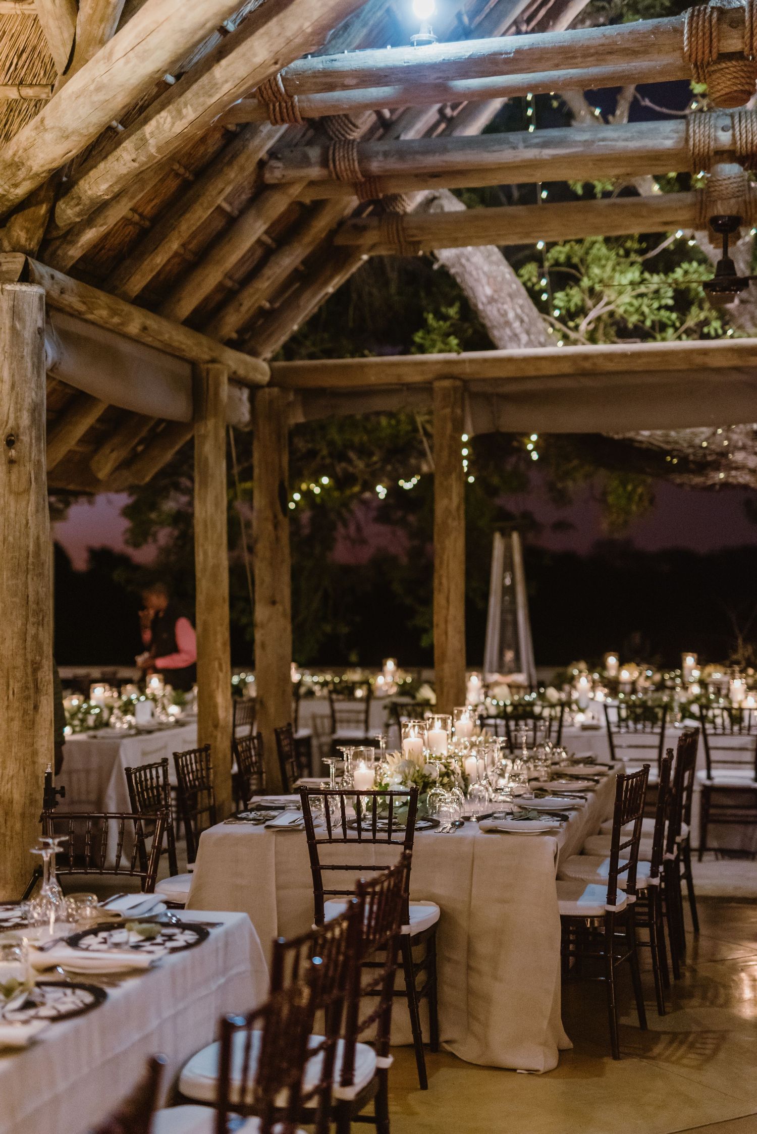 Rustic barn wedding venue with wooden beams and elegant table settings illuminated by string lights.