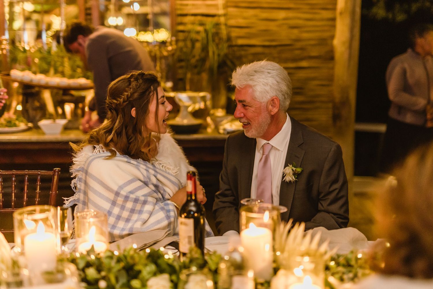Elegant dinner tables set with glowing candles and floral arrangements in a rustic barn setting.