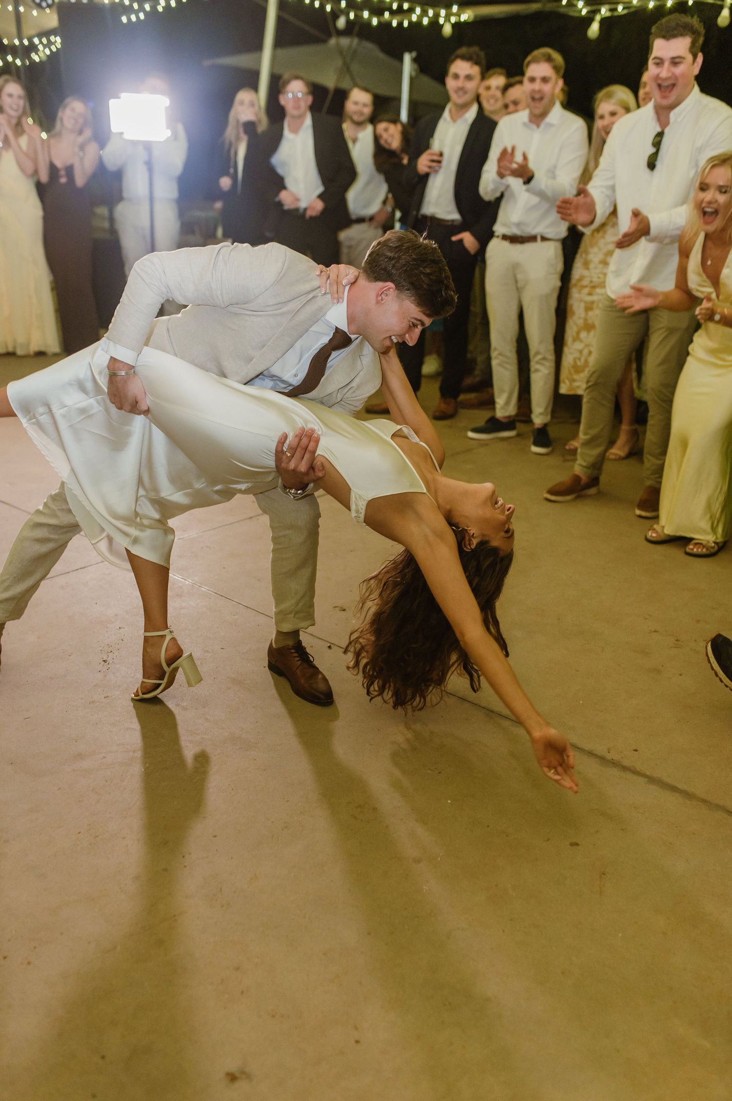 A couple performs a dramatic dip move while dancing under twinkling lights at a wedding reception.