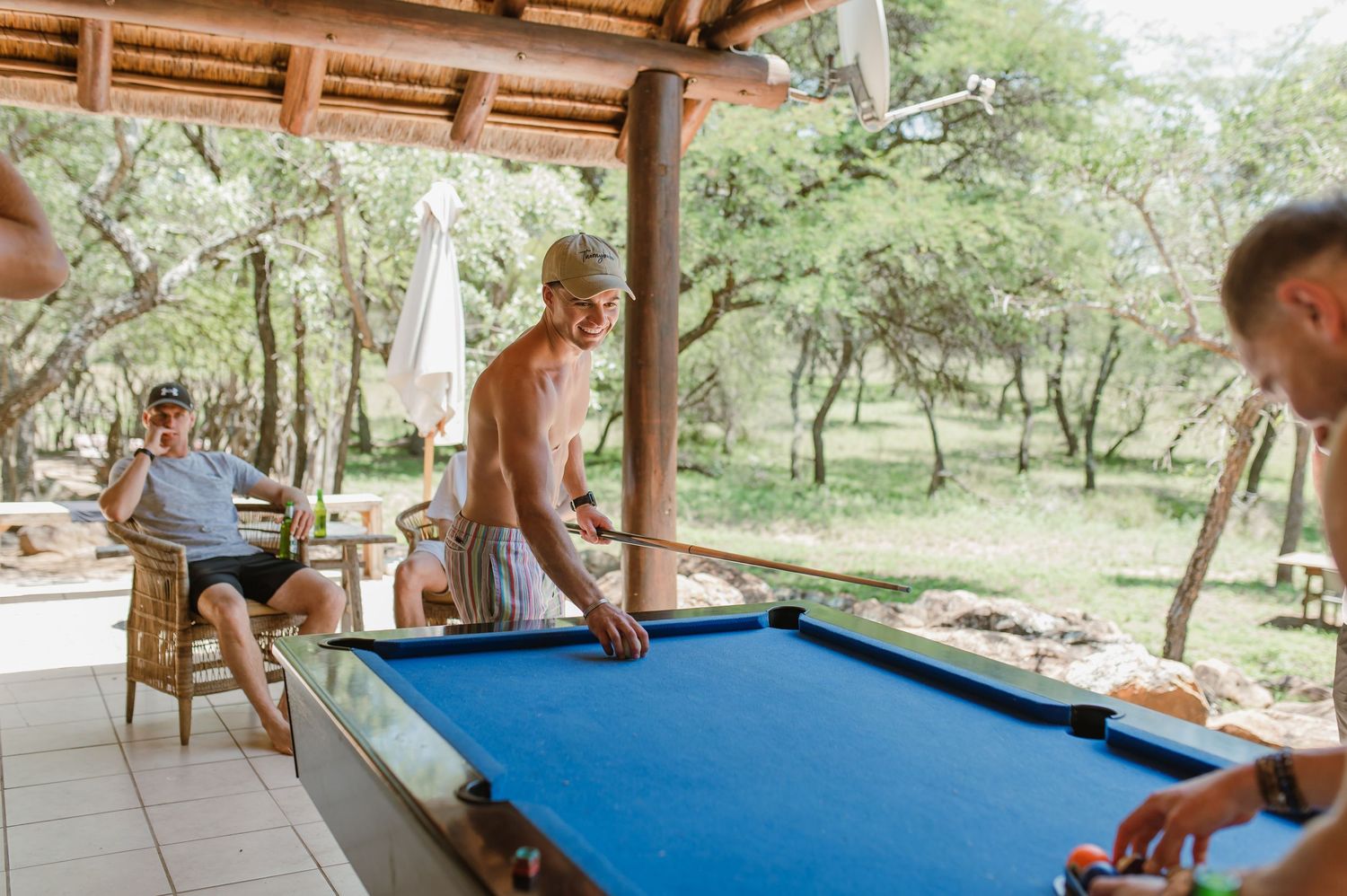 Friends gathered around a blue pool table under a covered outdoor patio.
