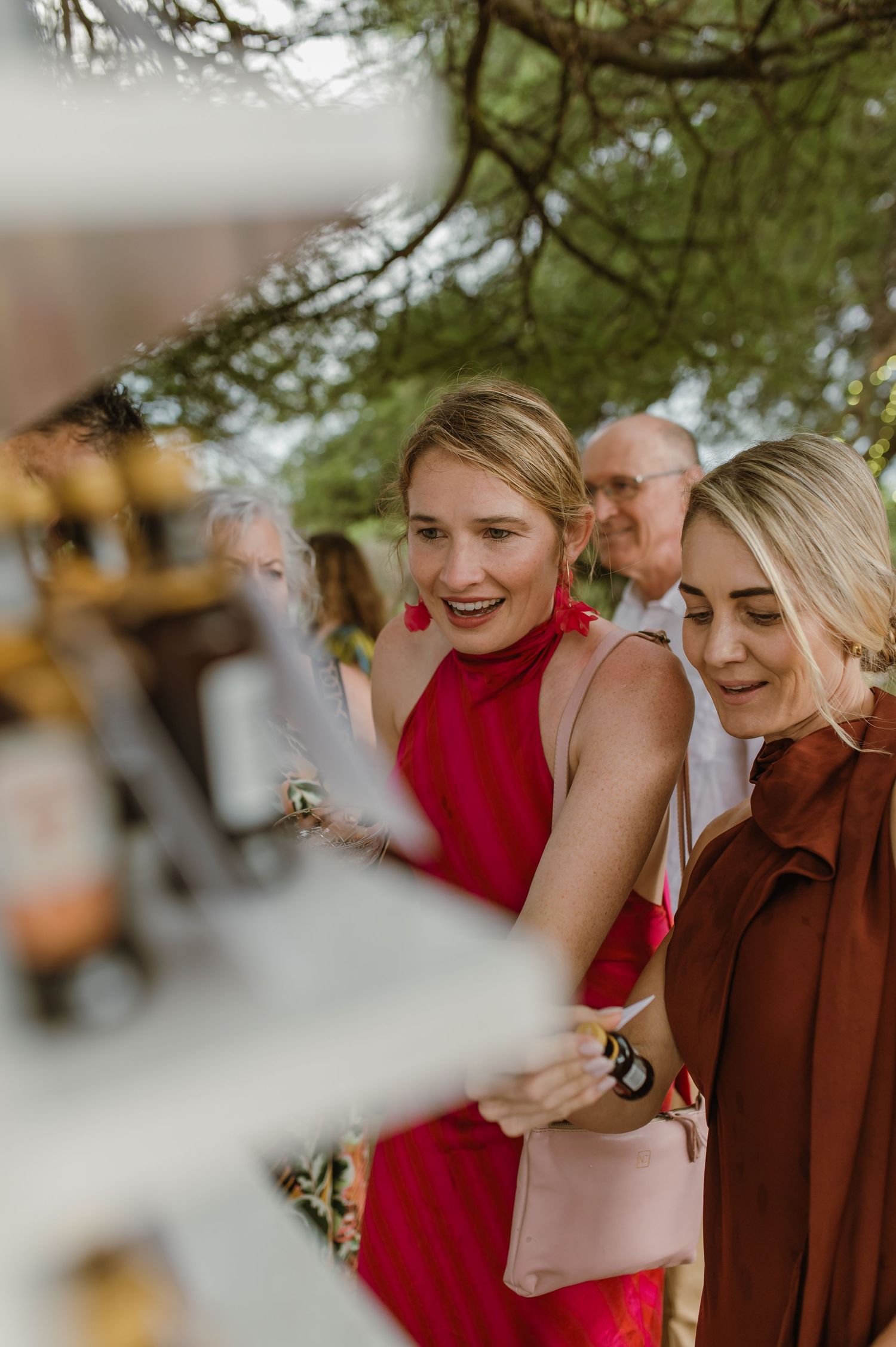 Guests enjoying candid moments at an outdoor wedding celebration under tree branches.