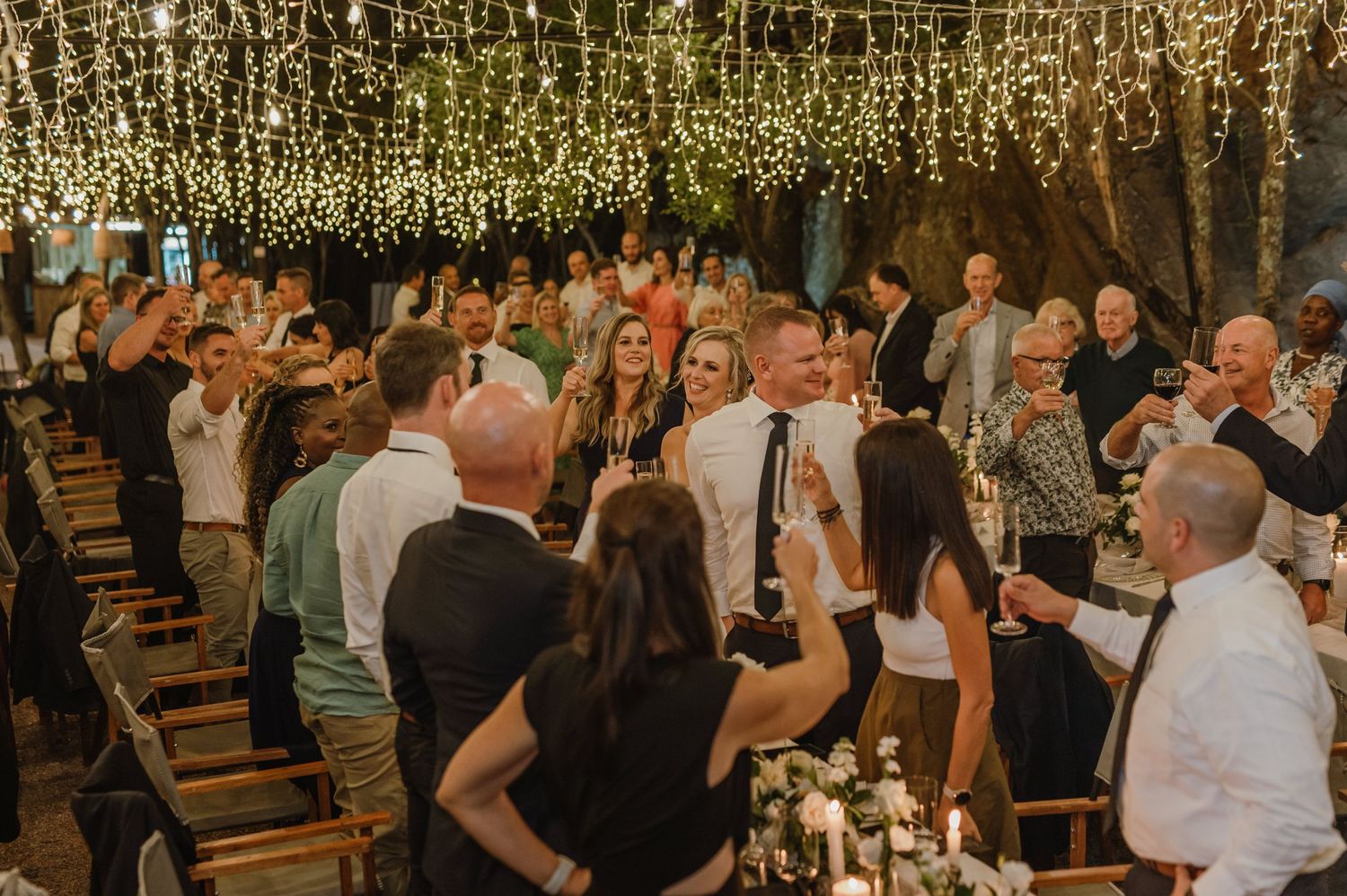 Wedding guests enjoying a festive celebration under romantic fairy light canopy.
