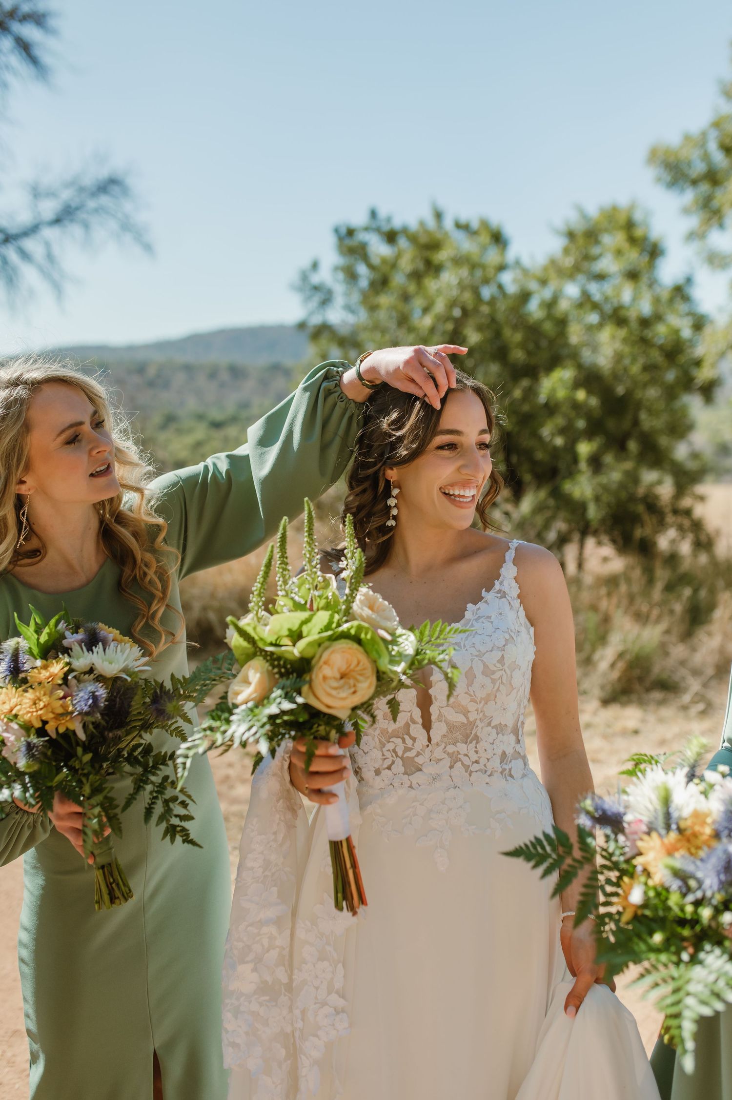 Bridal party holds bouquets while sharing joyful moment in outdoor desert setting.