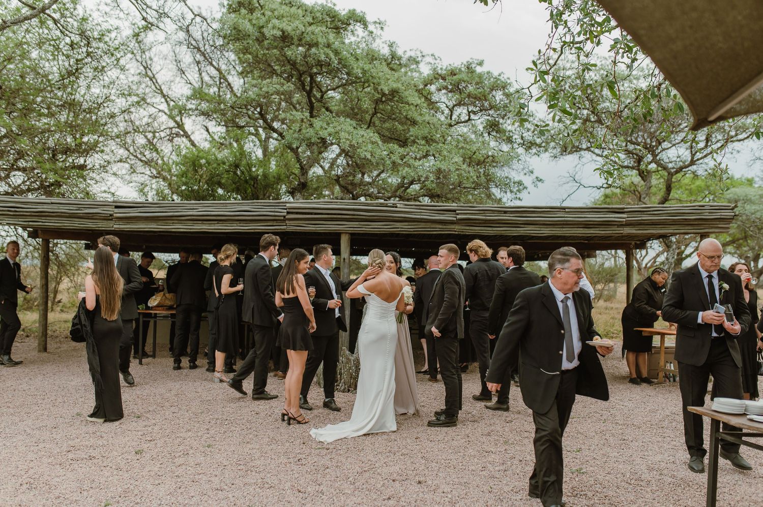 Outdoor wedding reception with guests mingling under trees.