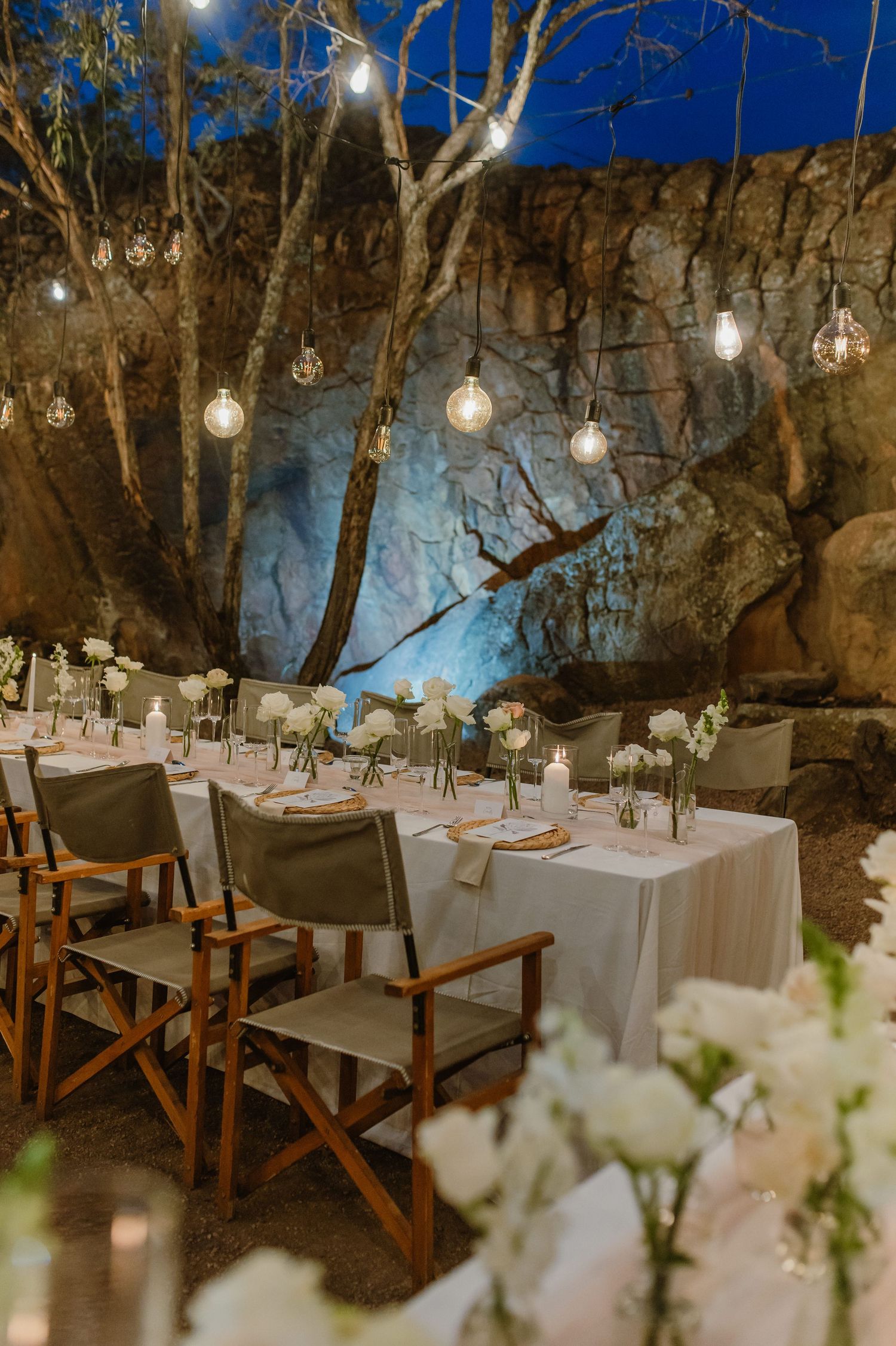 Intimate dining setup against rocky cave walls decorated with hanging lights and white floral arrangements.