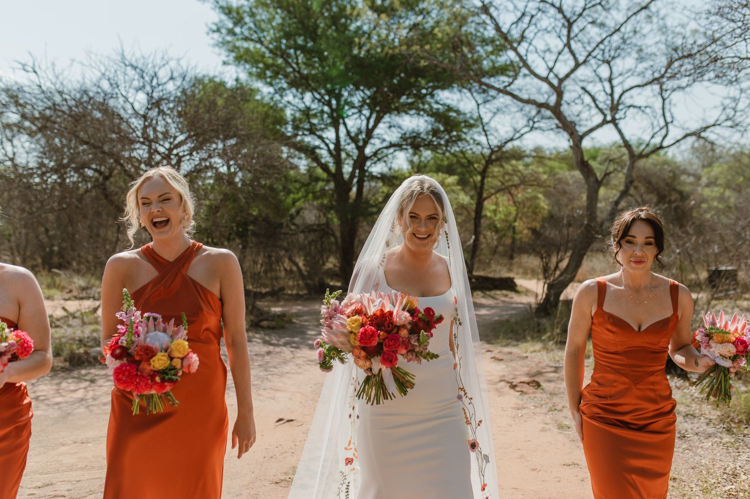 Wedding party holding vibrant red and orange bouquets against desert backdrop.