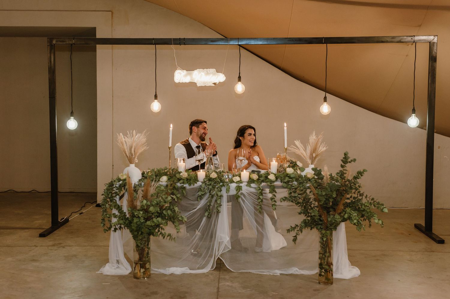 Elegant wedding reception setup with floral arrangements and string lights under white tent.