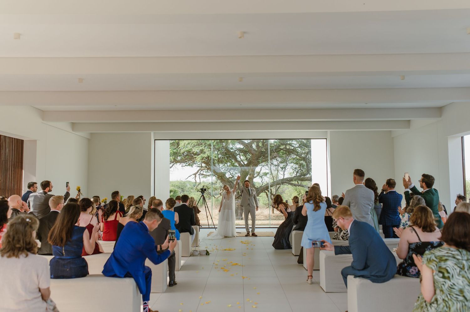 Panoramic view of wedding ceremony space with guests seated in modern white interior.