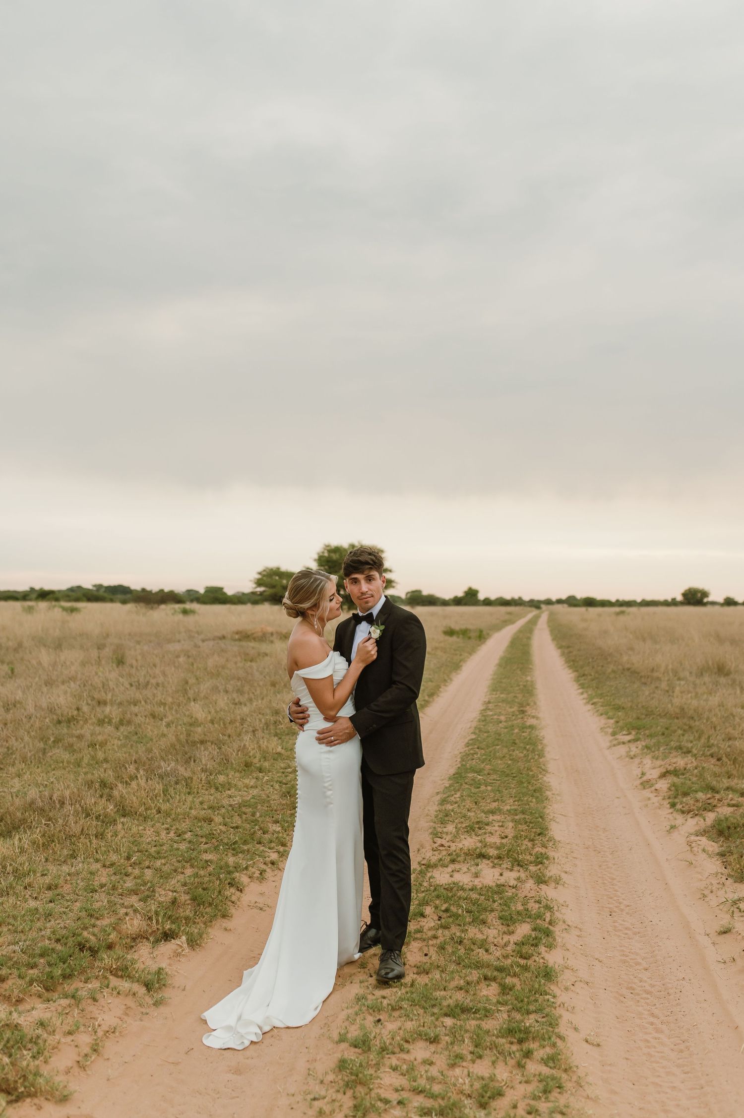 Wedding couple sharing intimate moments along a rural dirt road surrounded by grassland.