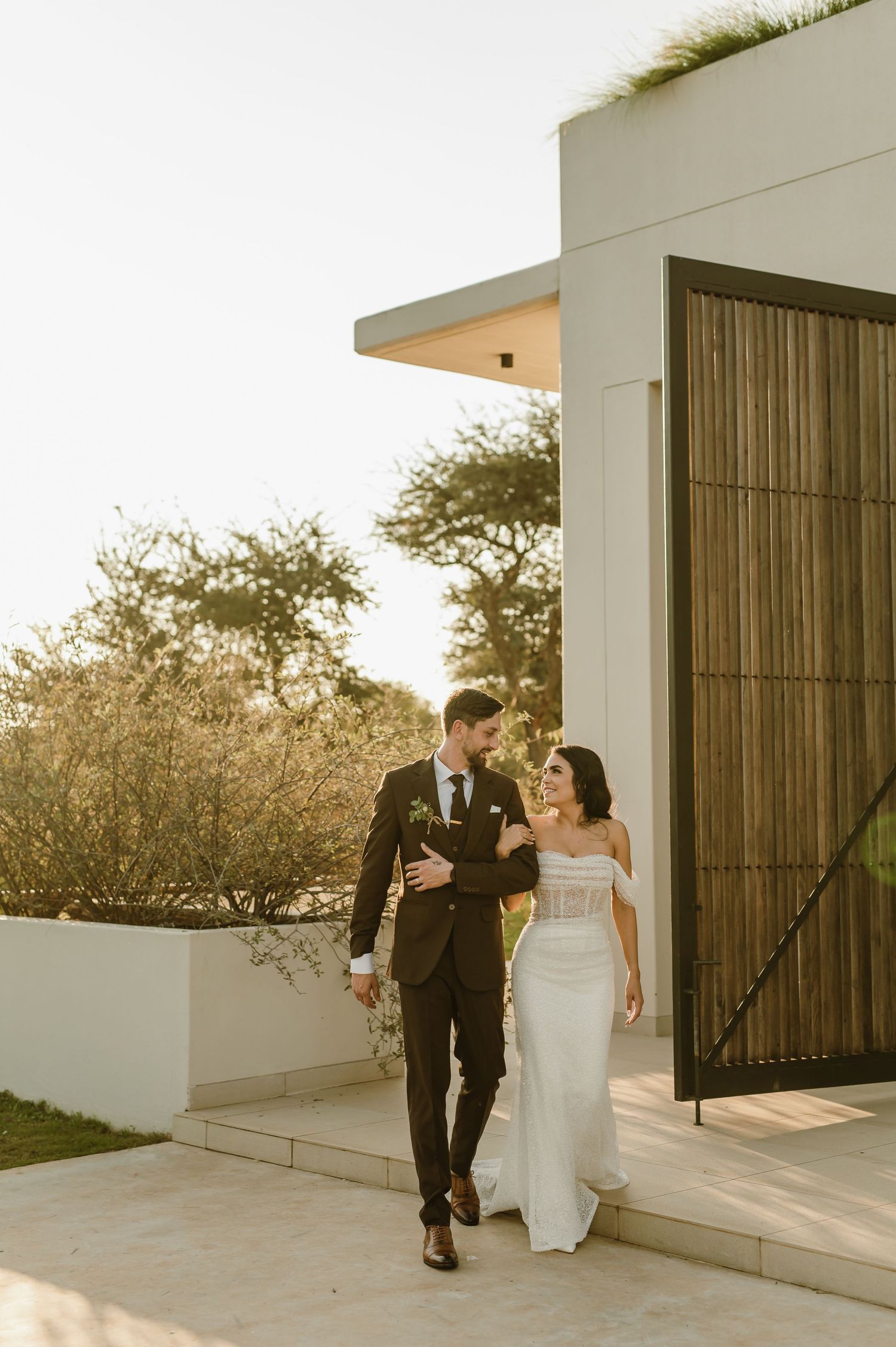 Wedding couple walks together on modern white balcony during sunset.