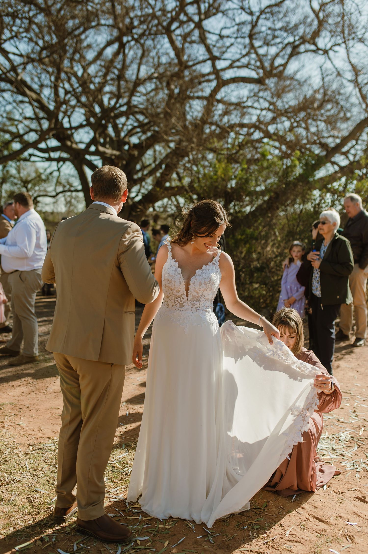 Wedding party gathered on natural terrain under sprawling tree branches.
