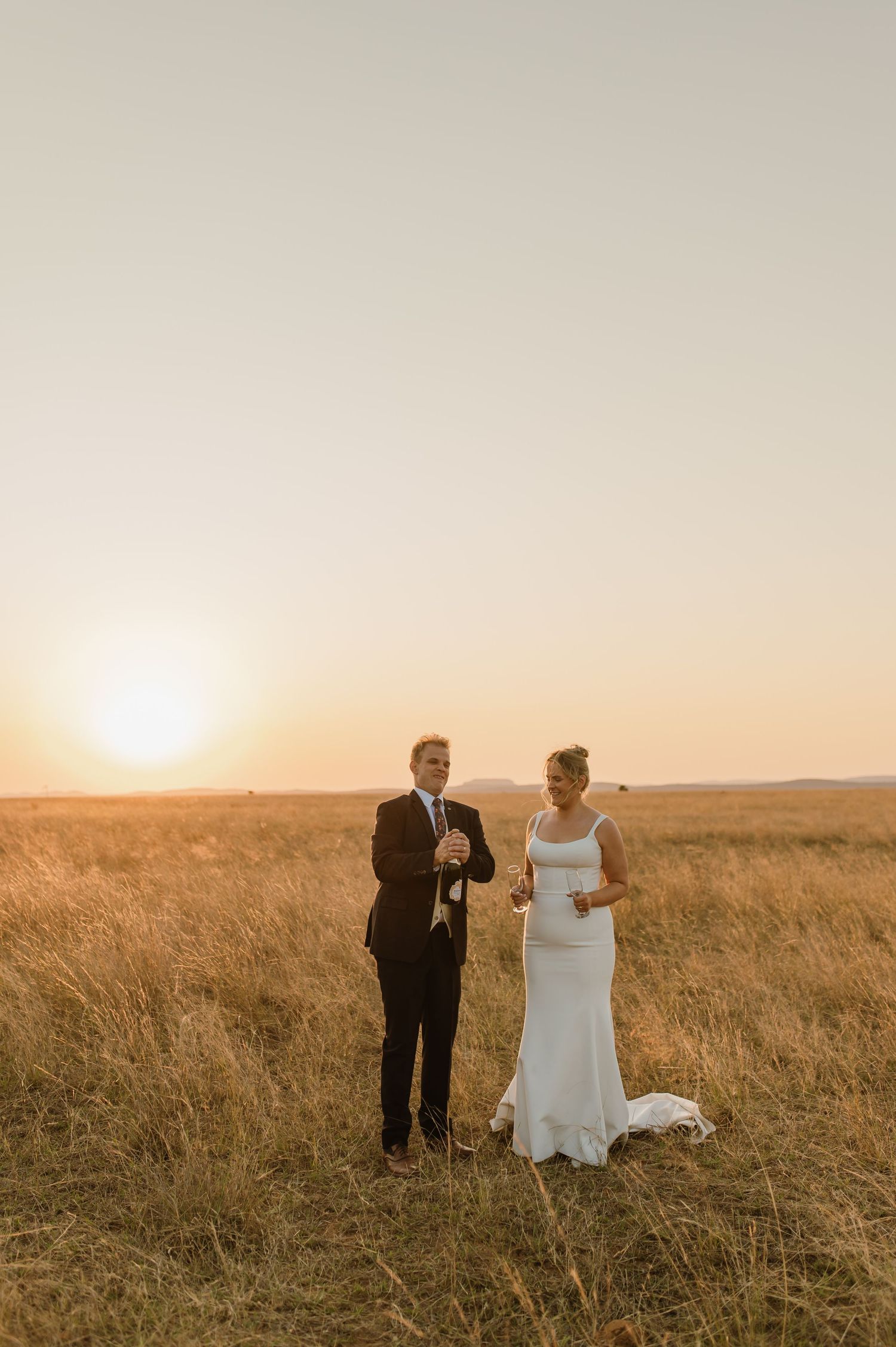 Wedding couple sharing candid moment in sunlit prairie landscape.