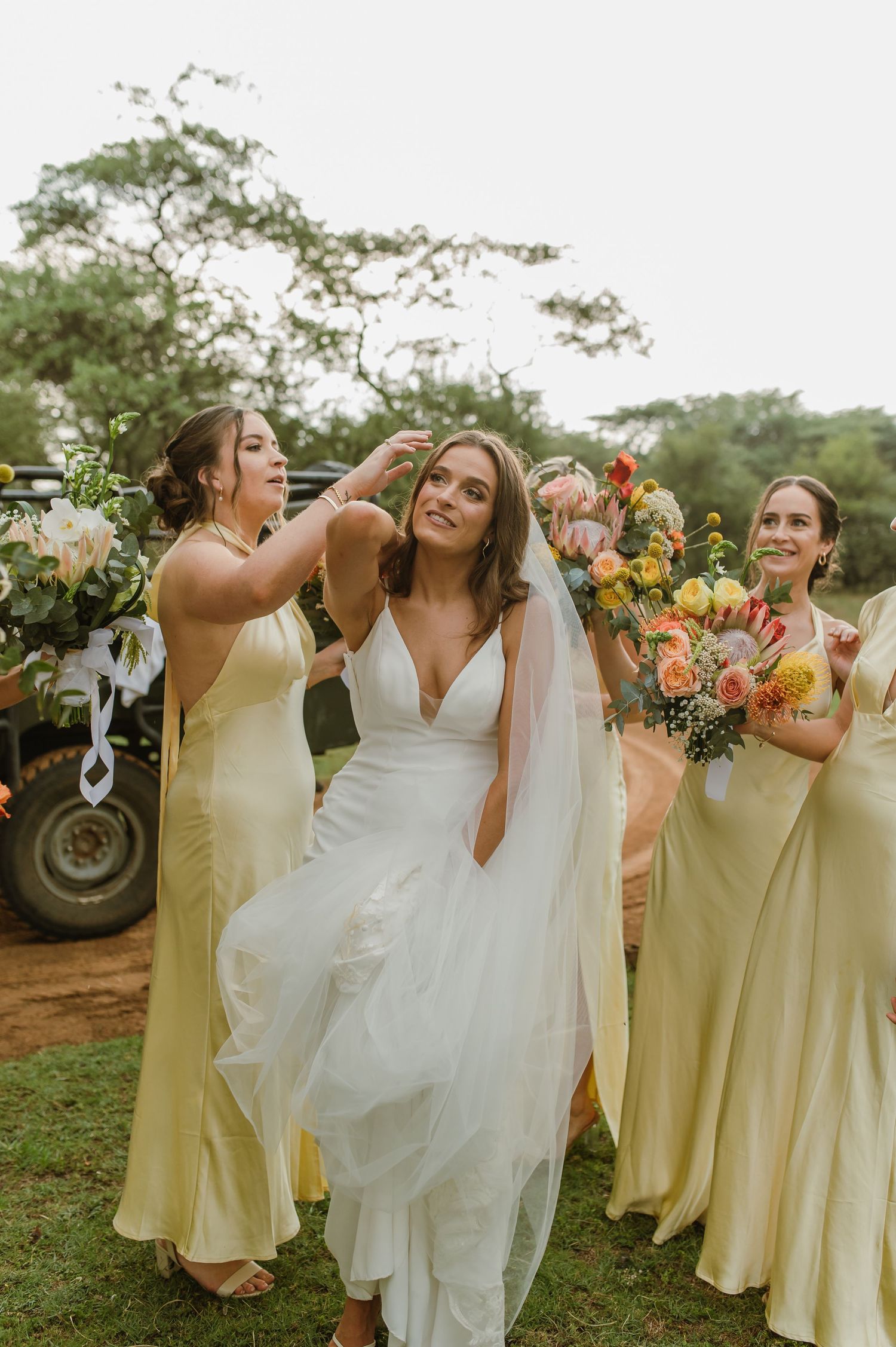 Bridal party in yellow dresses and white gown pose together outdoors with vibrant bouquets.