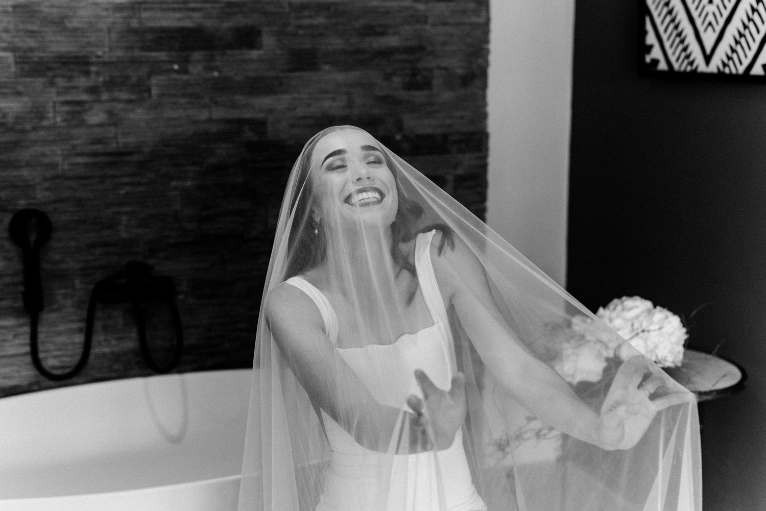 Wedding party laughs together during candid indoor photo session with exposed brick wall backdrop.