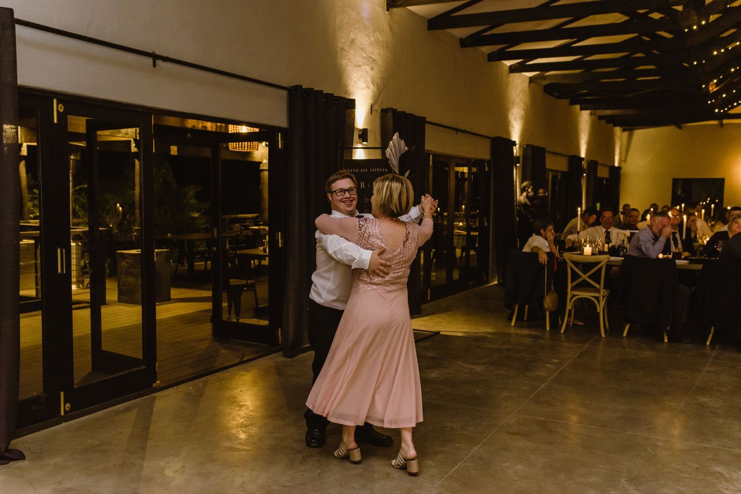Couples dancing together at an indoor venue with warm lighting and exposed wooden beams overhead.
