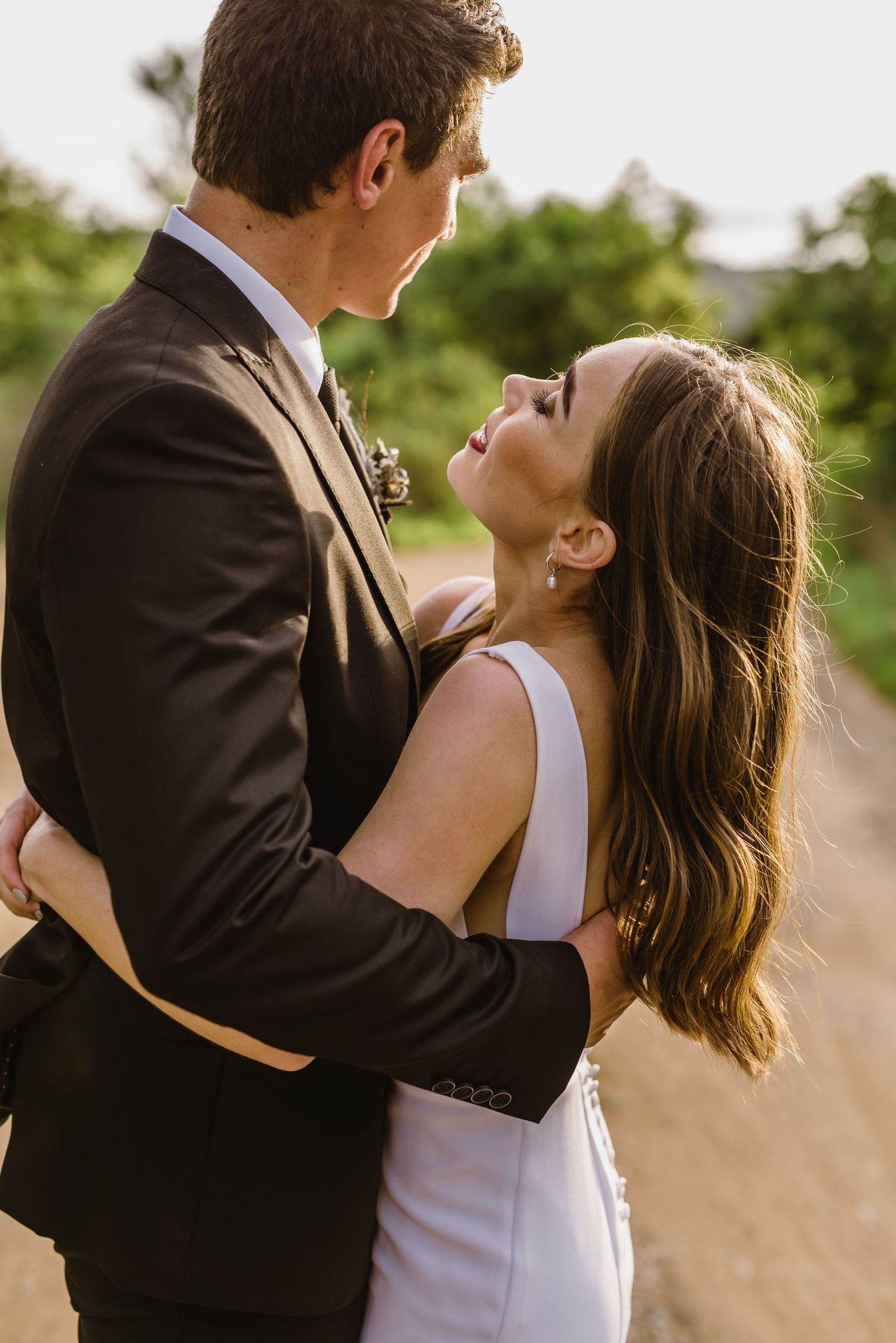 A tender embrace between newlyweds on a rustic outdoor path at sunset.
