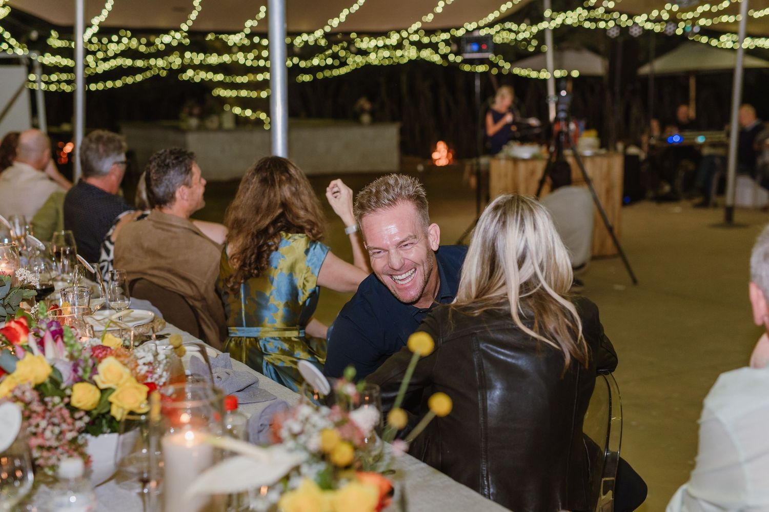 Guests mingle and dine at an evening wedding reception under a tent with string light decorations.