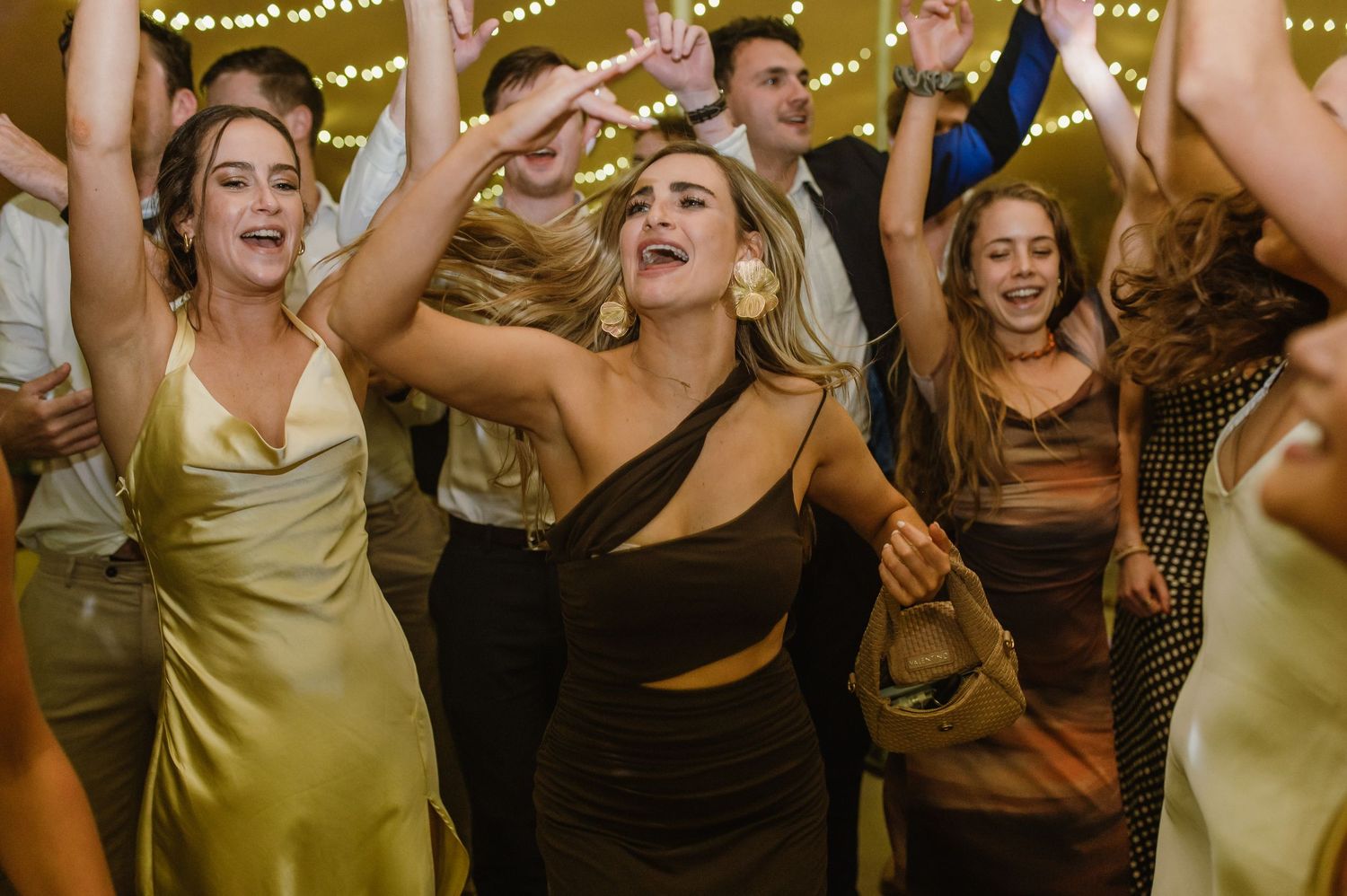 Wedding reception dance floor filled with guests celebrating under string light decor.