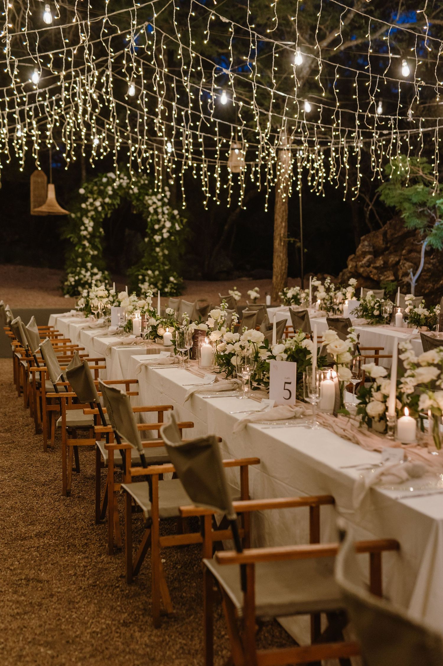 Long banquet tables set under canopy of string lights for outdoor wedding reception.