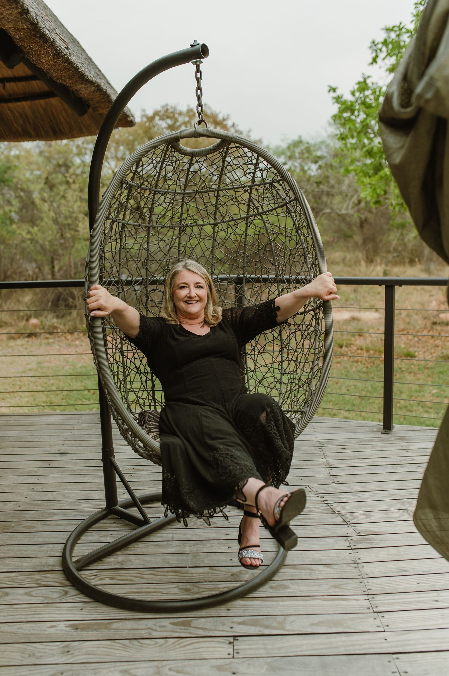 Person relaxing in hanging egg chair on wooden deck of safari lodge.
