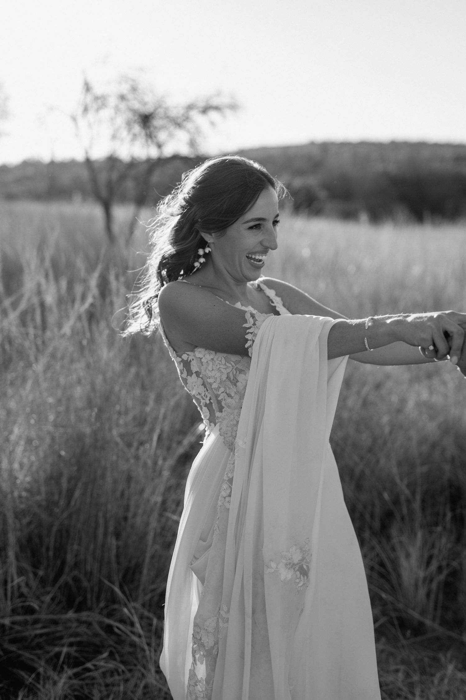 Black and white portrait of bride in flowing dress against natural field backdrop.
