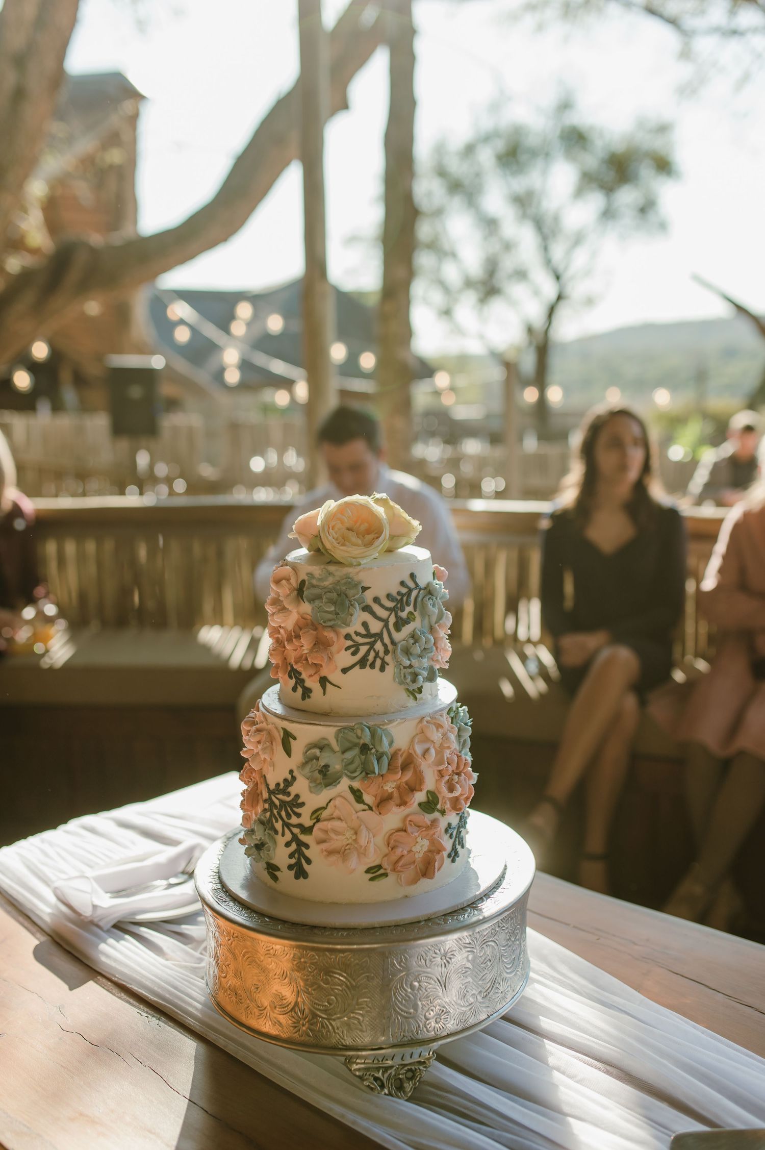 Elegant two-tier wedding cake with floral decorations displayed on white wooden table.