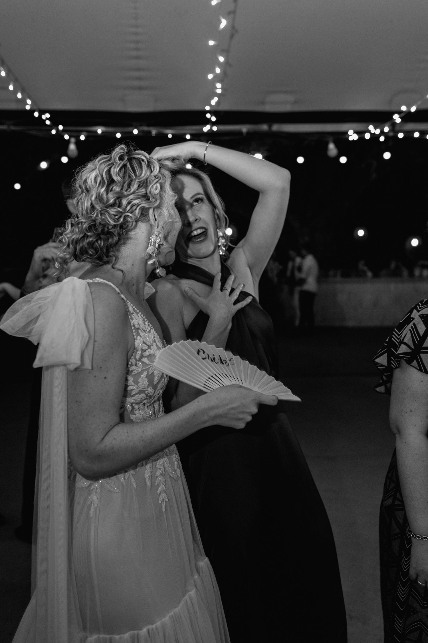 Black and white photo of dancers with string lights overhead at a wedding reception.