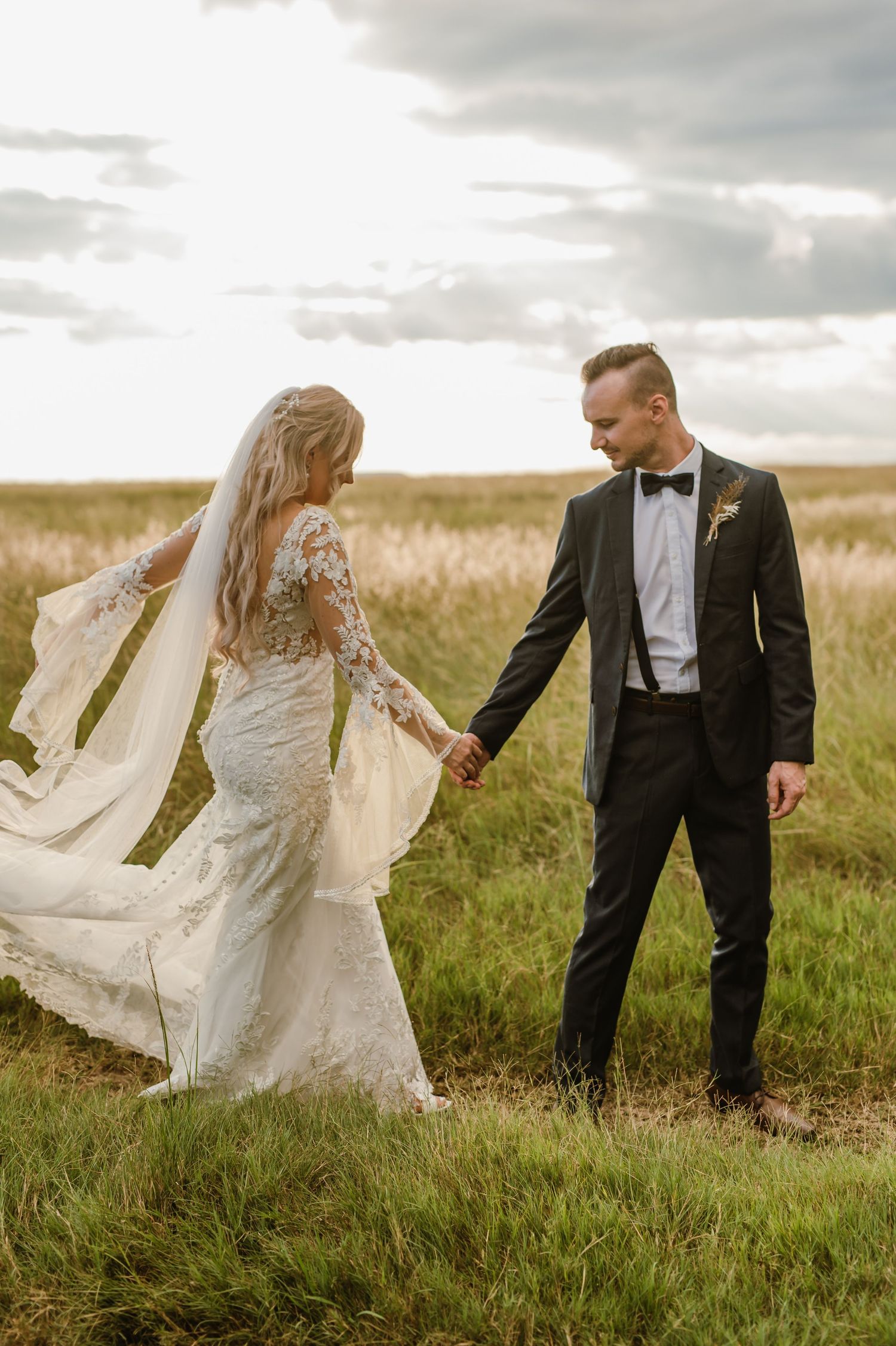 Bride and groom share a romantic moment in a windswept prairie field.