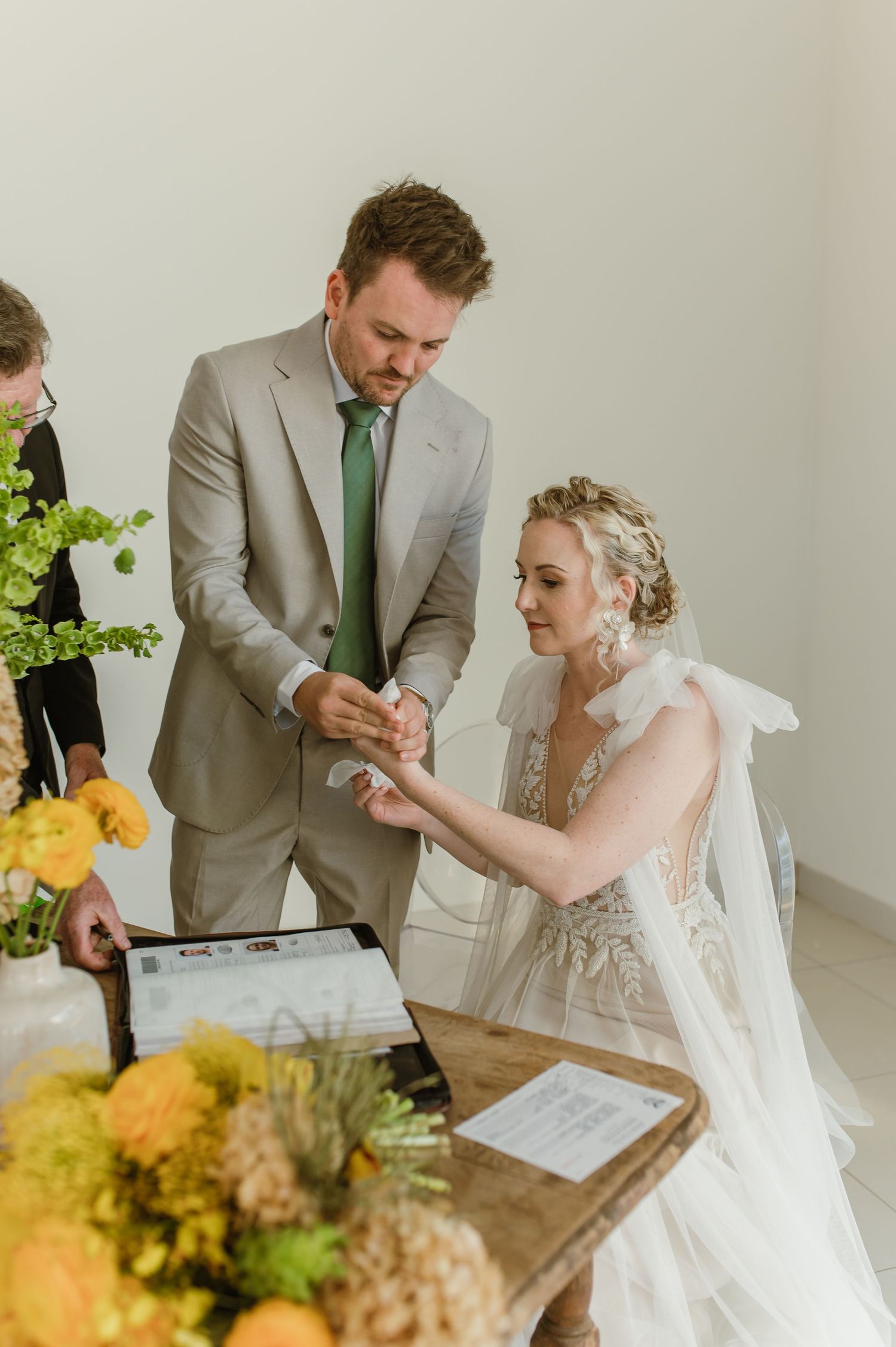 Couple reviewing wedding documents at wooden table decorated with yellow flowers.