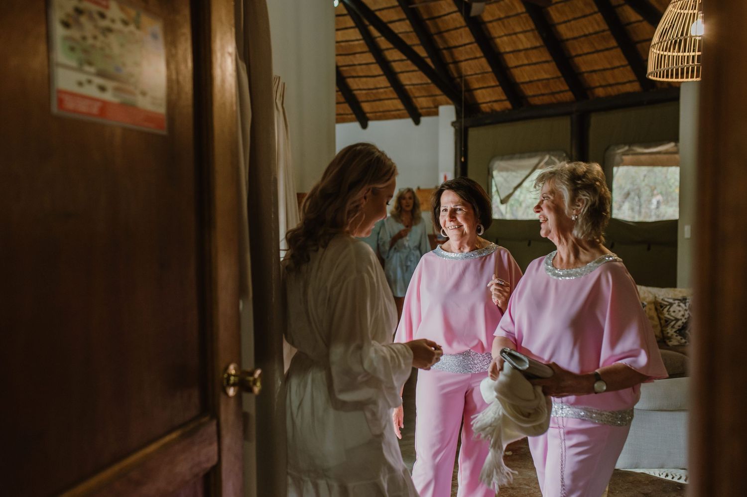 Group wearing pink robes gathered in rustic venue during wedding preparations.