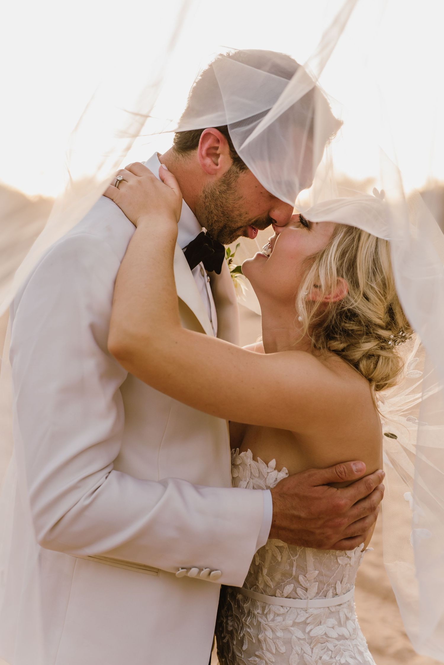 Tender moment between newlyweds sharing a romantic kiss in soft sunlight.