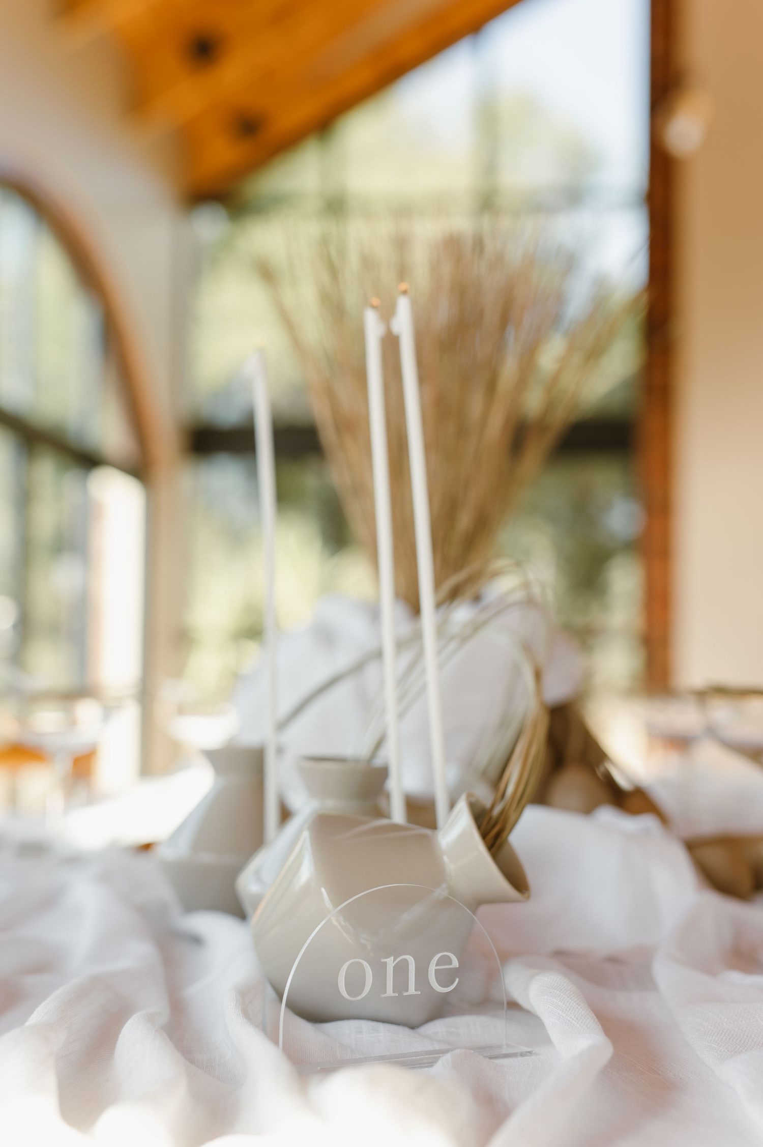 White wedding reception decor with candles and soft textiles in sunlit venue.