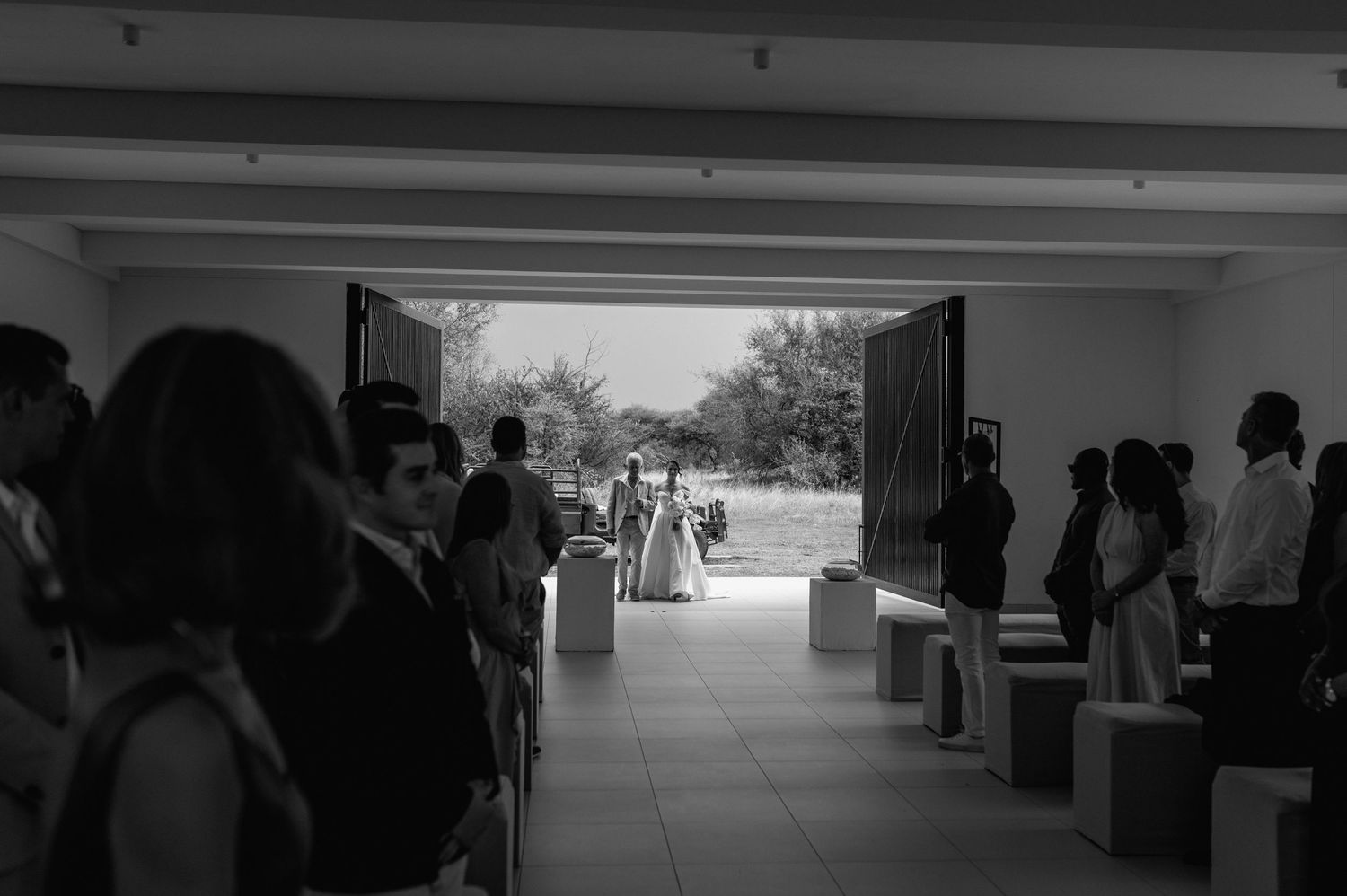 A silhouetted wedding party stands in a minimalist architectural space with dramatic lighting.