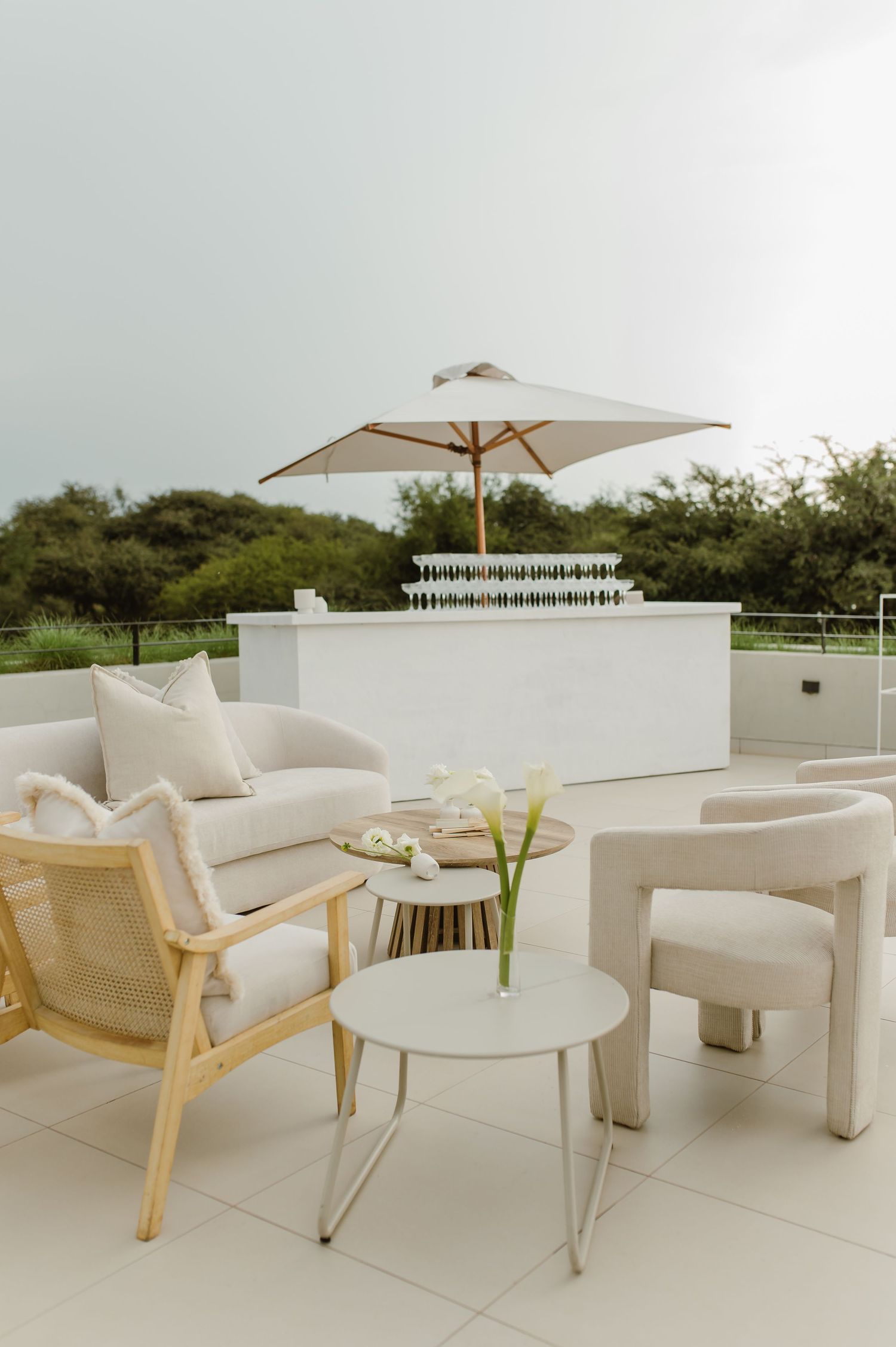 Modern outdoor lounge area with white cushioned furniture and umbrellas arranged on a patio overlooking greenery.