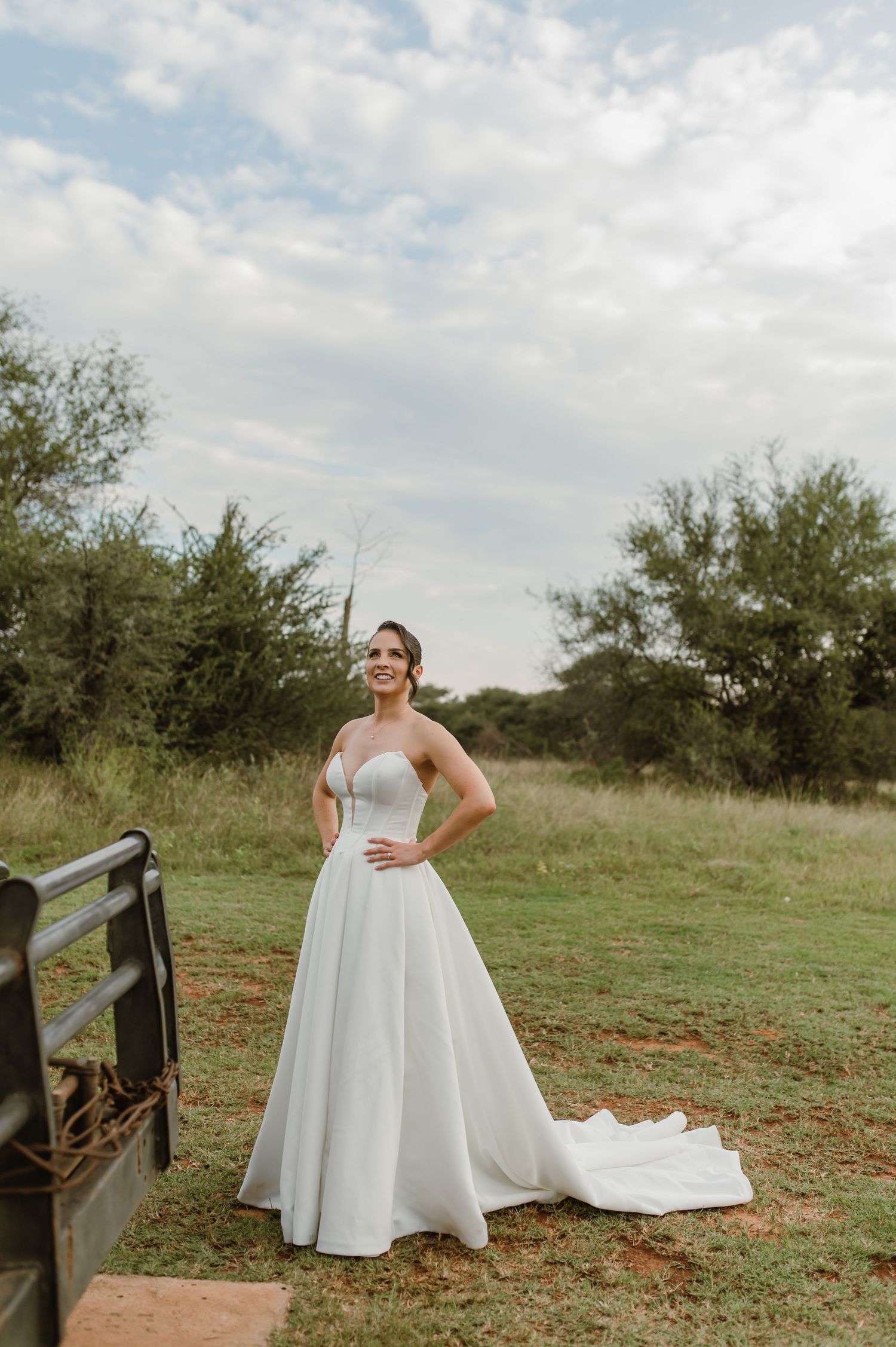 A beautiful white wedding dress flows in a rustic outdoor setting with green grass and trees in the background.