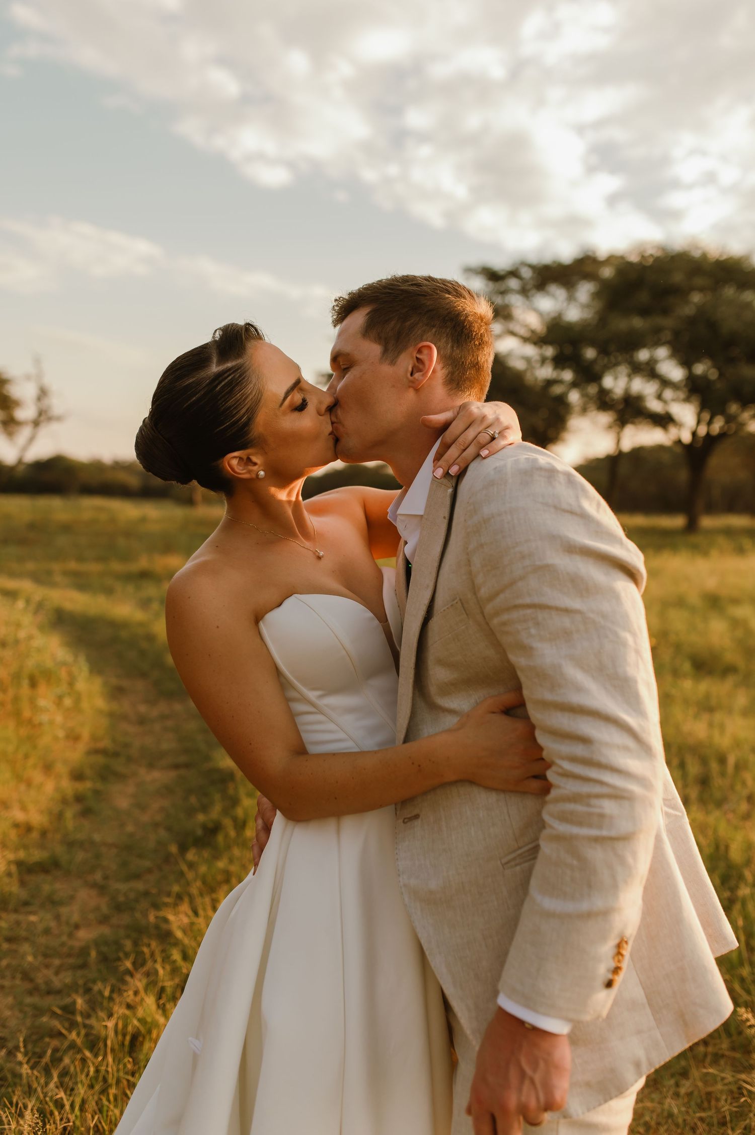 Intimate wedding portraits of couple kissing during golden hour in a rustic outdoor setting.