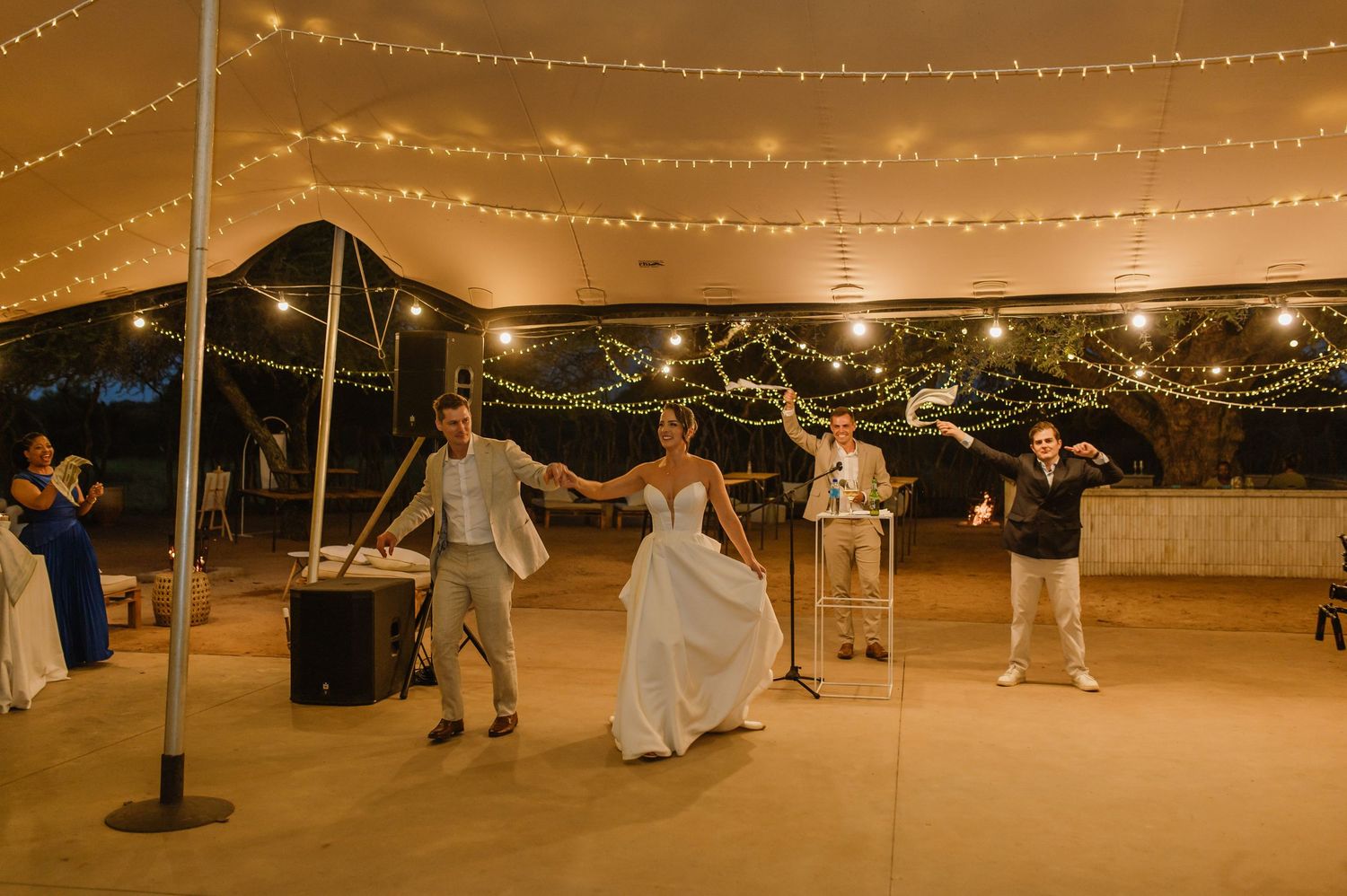 Wedding guests dancing under strung lights at an outdoor evening reception.