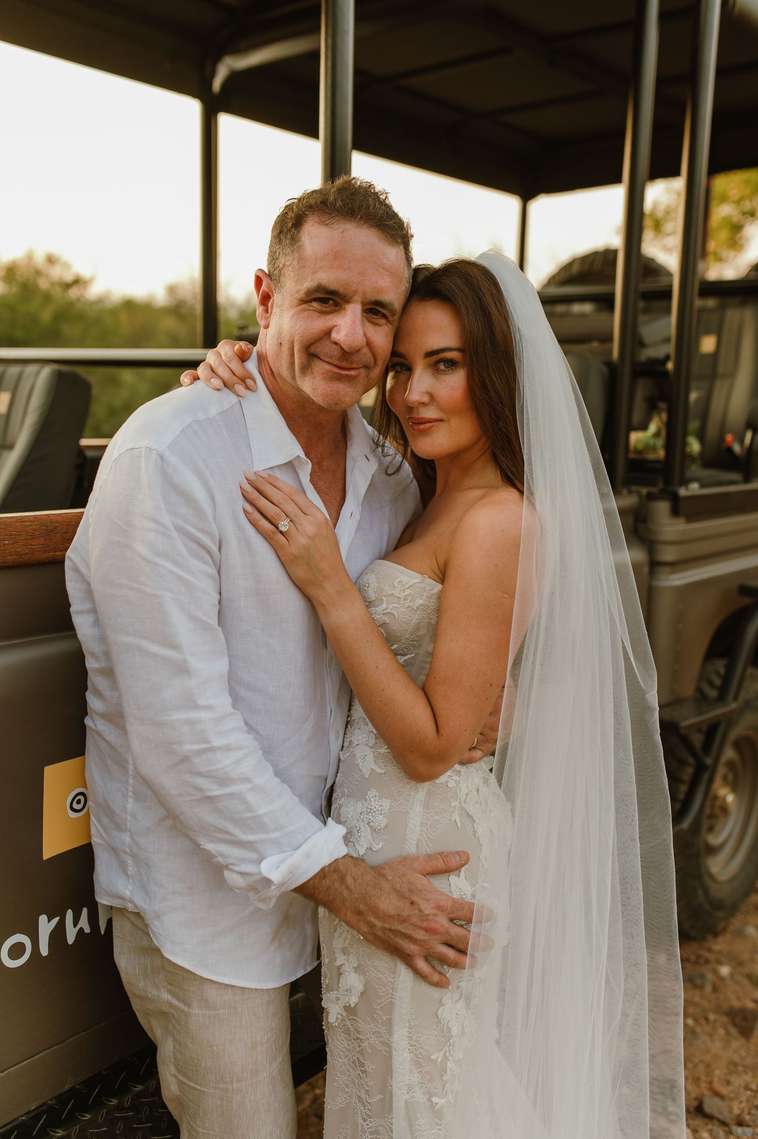 Smiling bride and groom posing together beside a safari vehicle at a bush wedding.