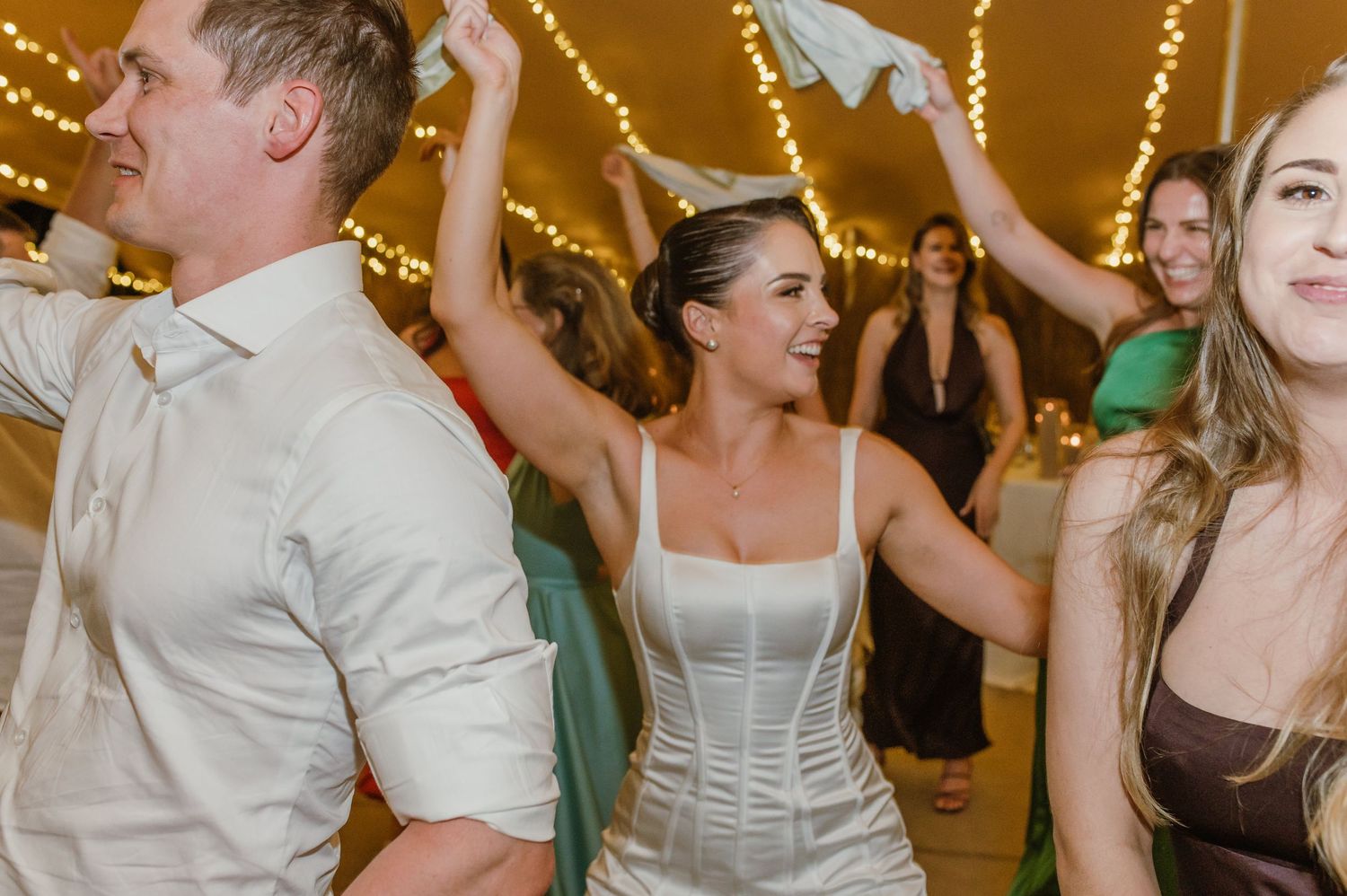 Lively dance floor filled with wedding guests under warm string light decorations.