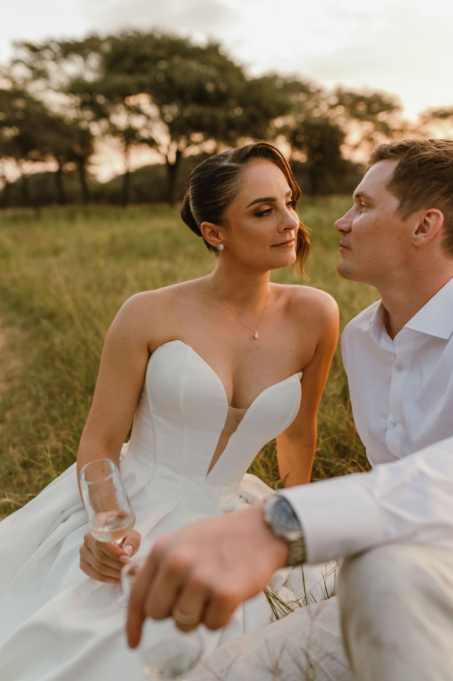 A romantic couple in wedding attire share an intimate moment in a sun-drenched field at golden hour.