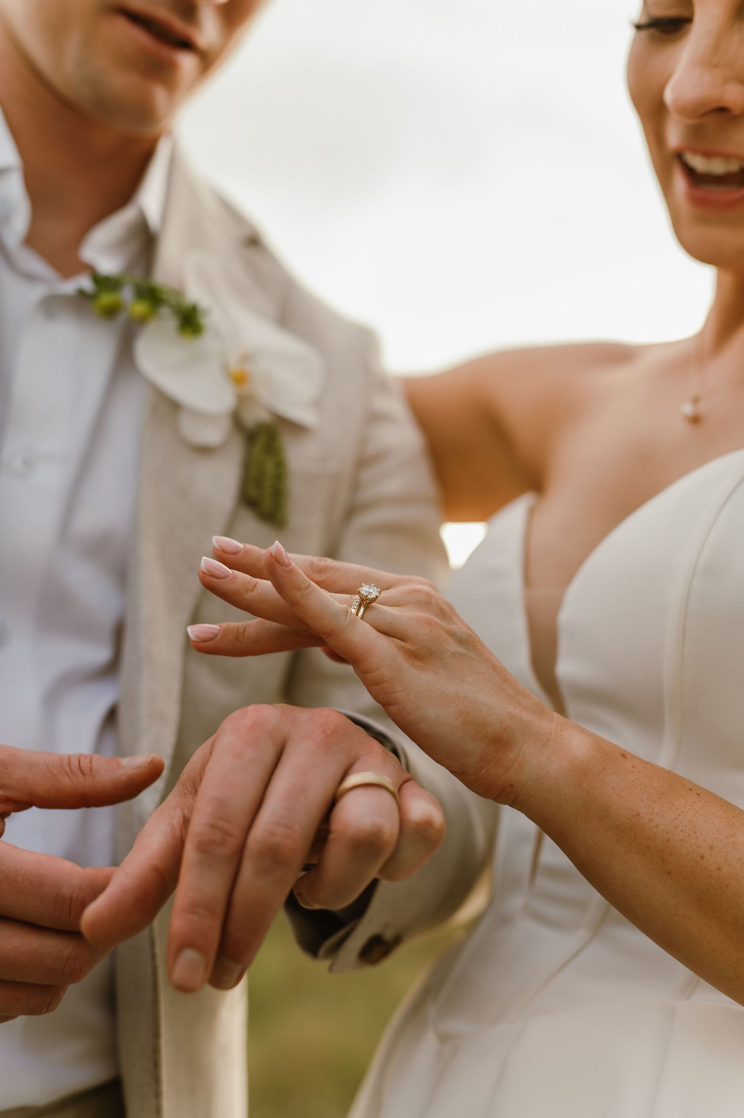 Close-up of hands exchanging wedding rings during an outdoor ceremony.
