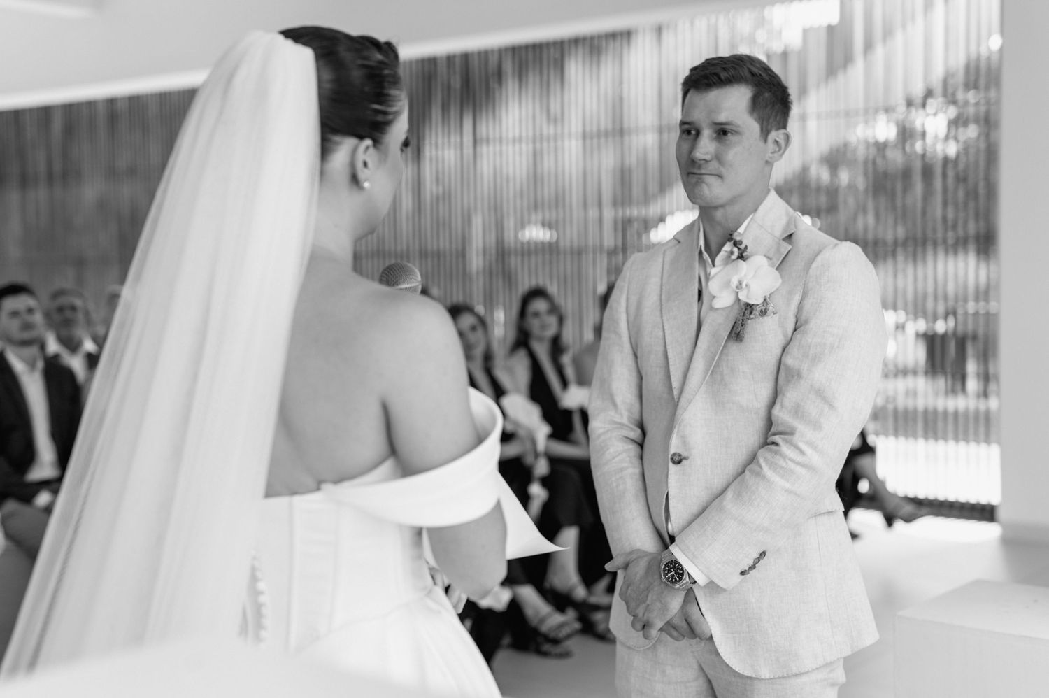 A black and white photo capturing an intimate wedding ceremony moment in a modern venue.